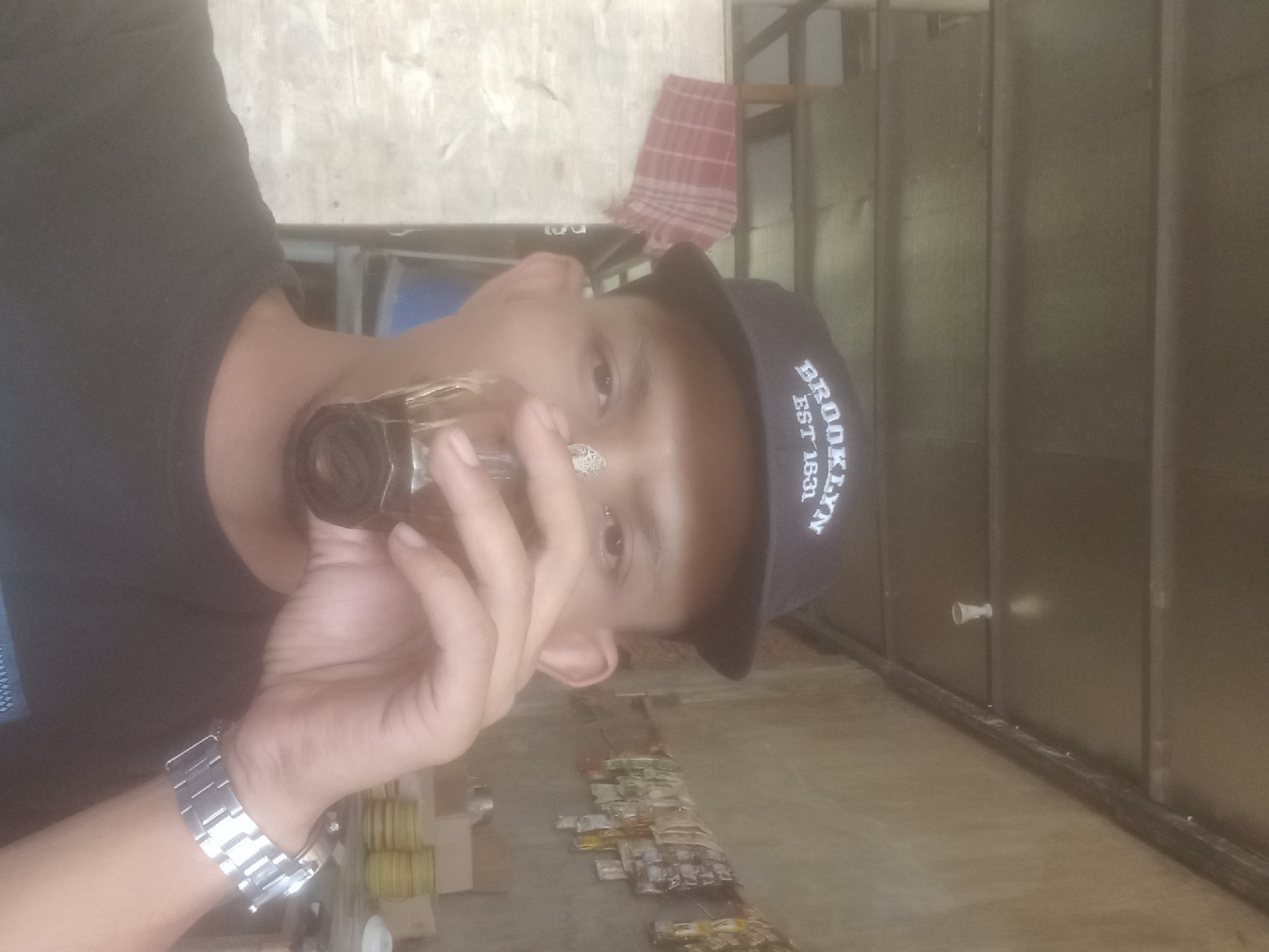 Sipping a dark drink in Keudejungkagajah, Brooklyn cap on