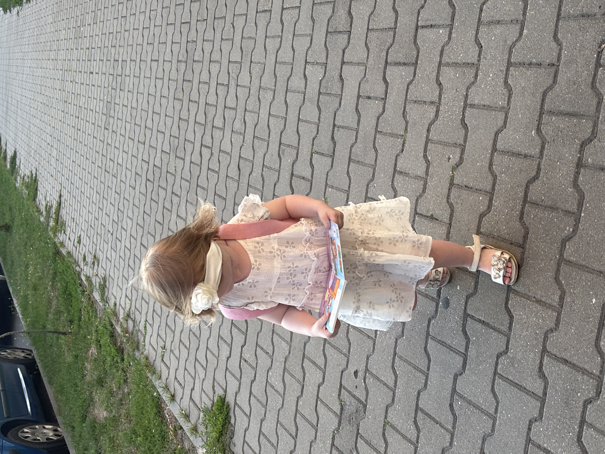 Child in white dress walks Brest sidewalk on a summer afternoon