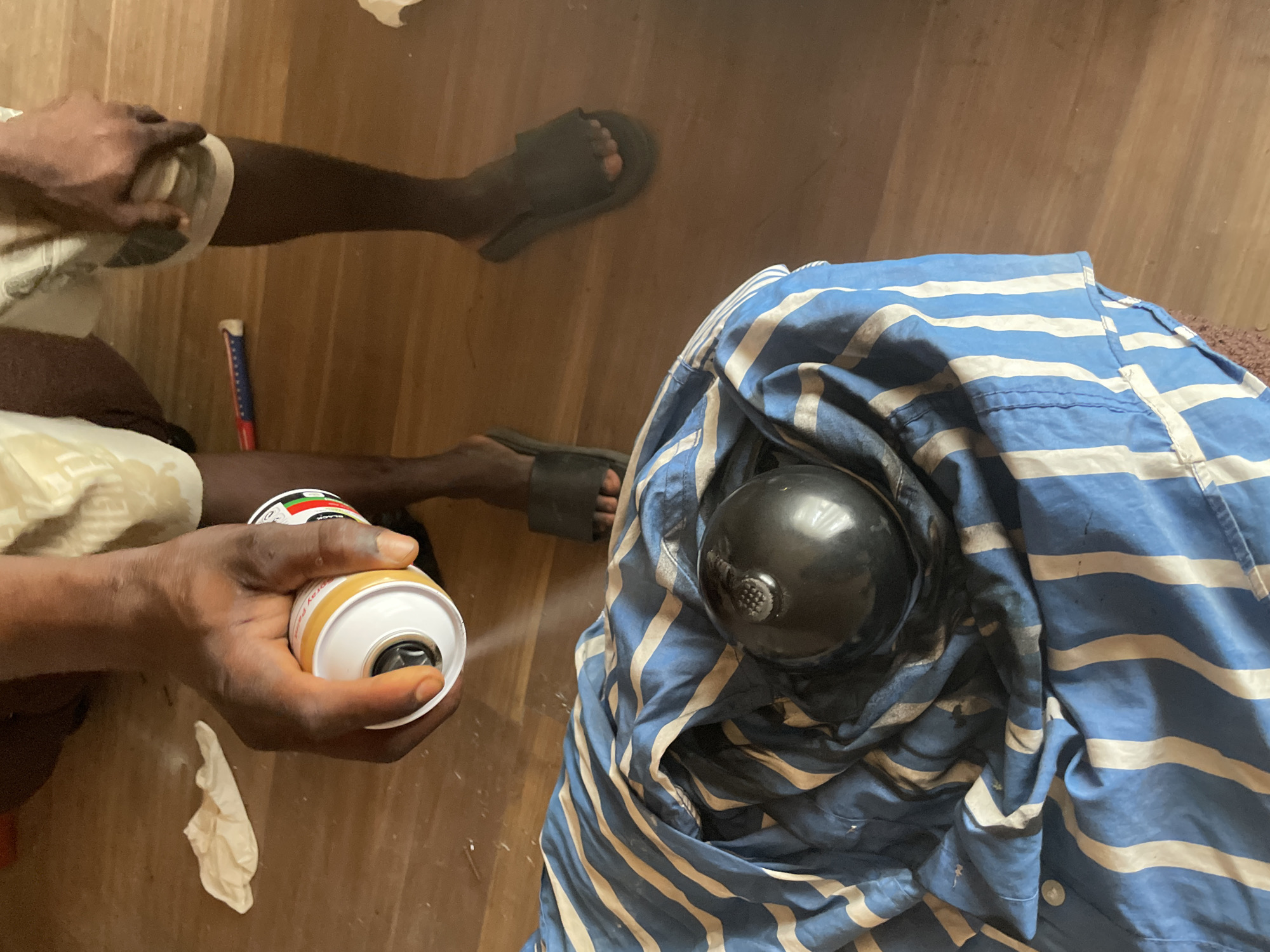 Person spray paints object on wooden floor in Ojomu