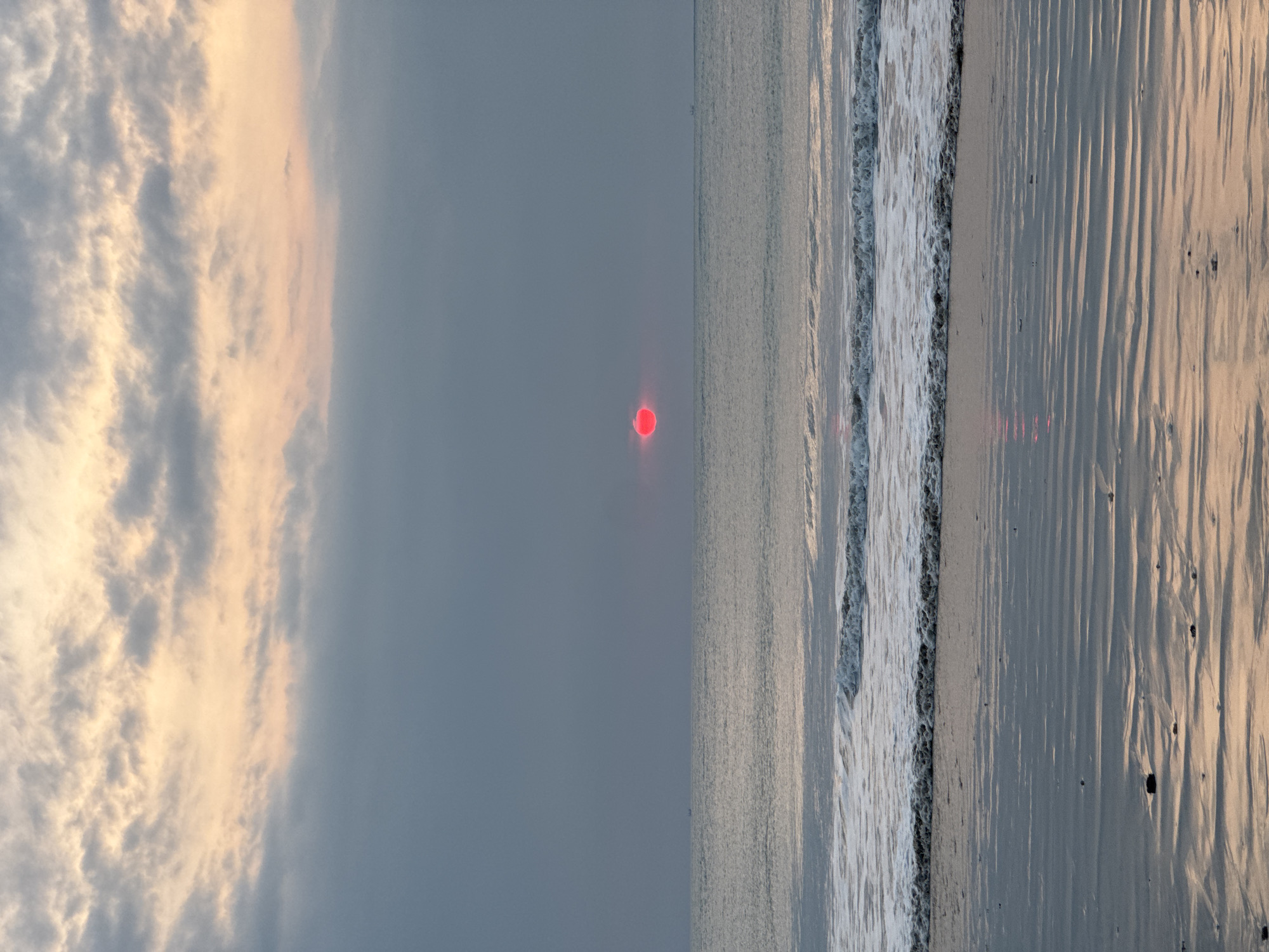 Red sun setting over Kuta Selatan beach, people at the shoreline