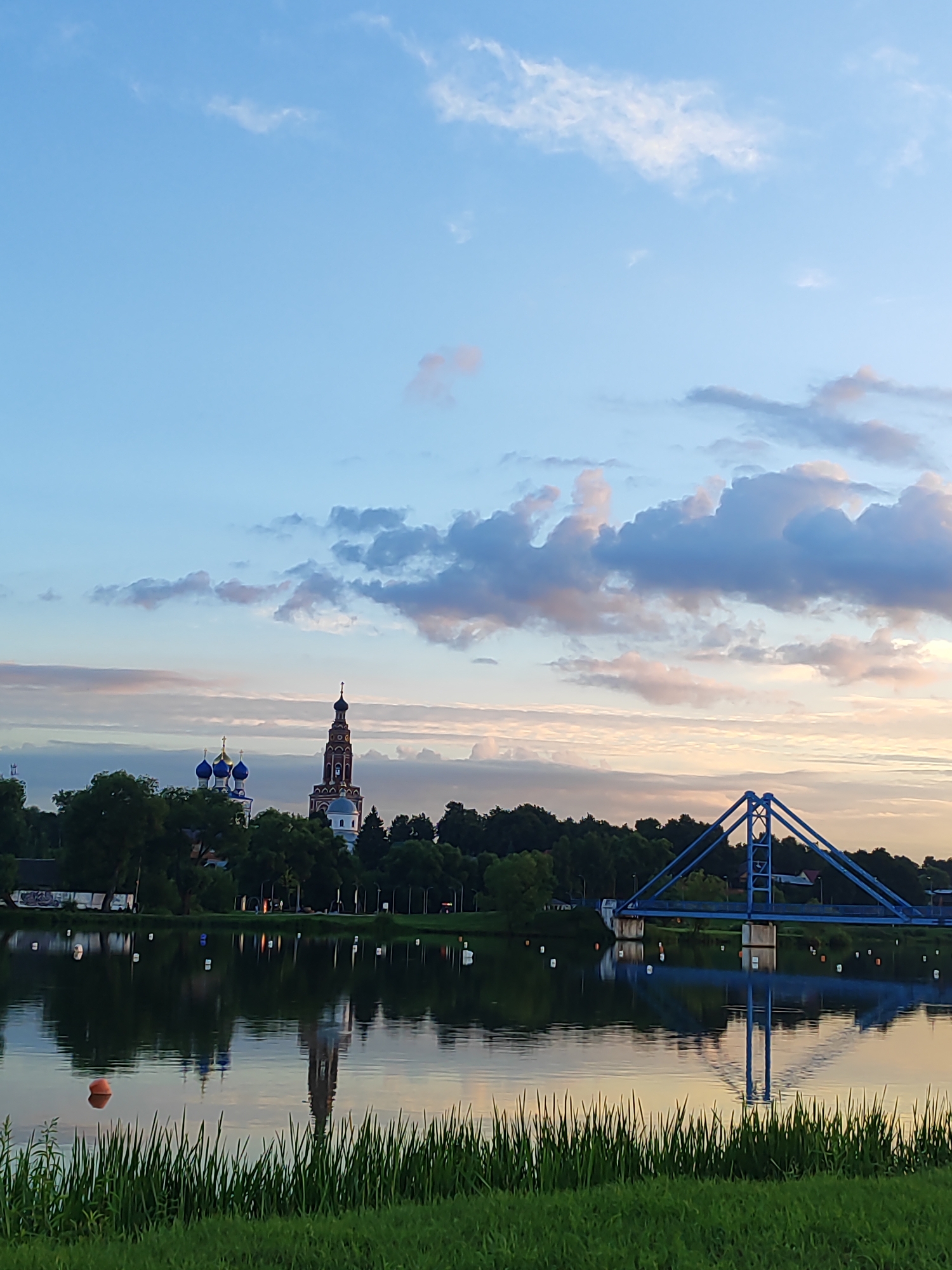 Blue pedestrian bridge over calm water at dusk, Bronnitsy
