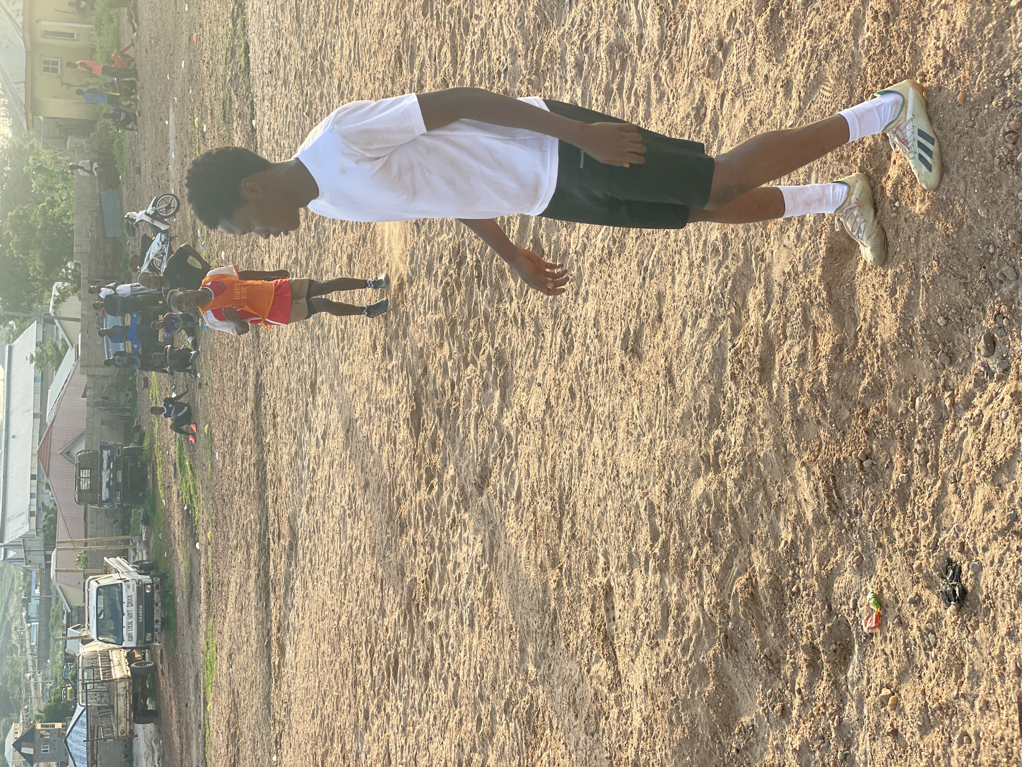 Pickup football on a sandy Lokoja field, late afternoon.