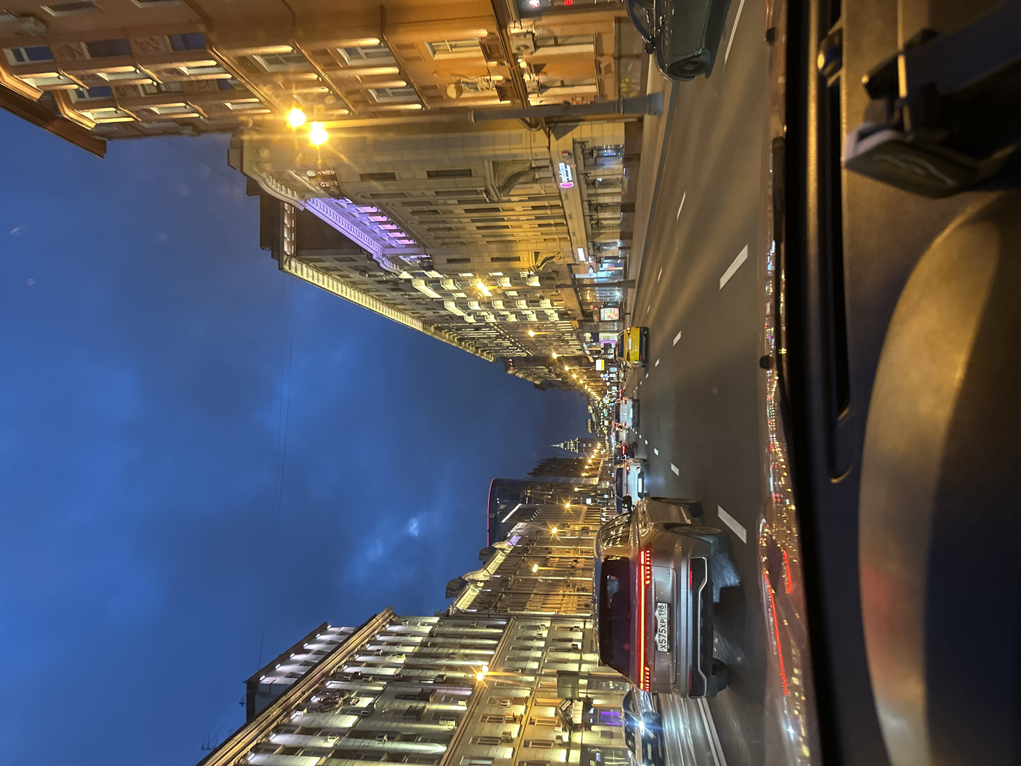 Cruising a lit city boulevard at dusk under heavy clouds