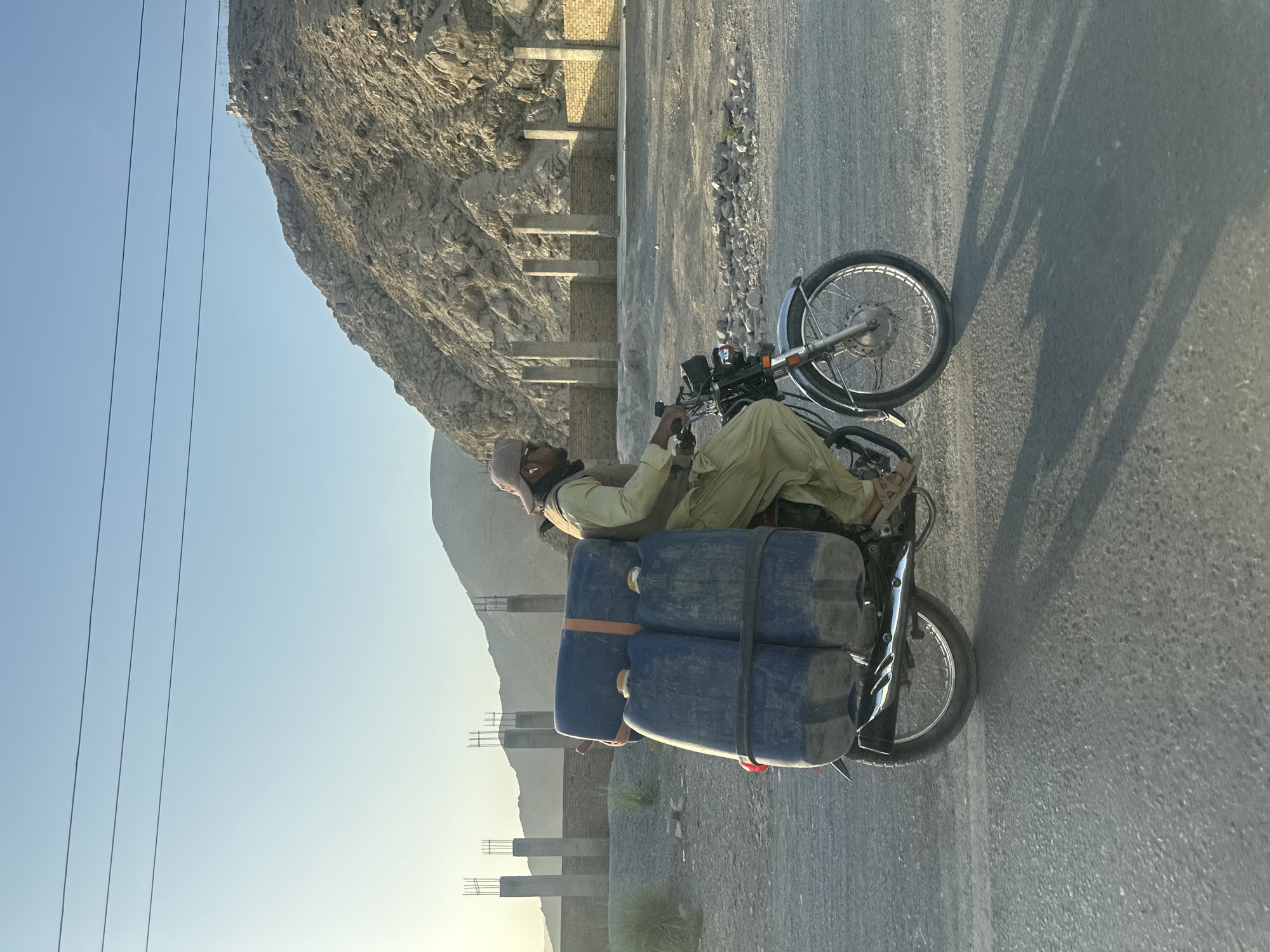 Motorcycle hauling blue liquid containers through Quetta streets
