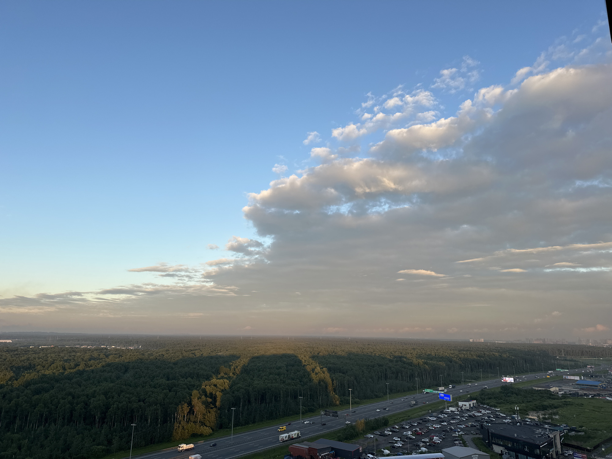 Kudrovo at golden hour: forest, highway, and apartment towers