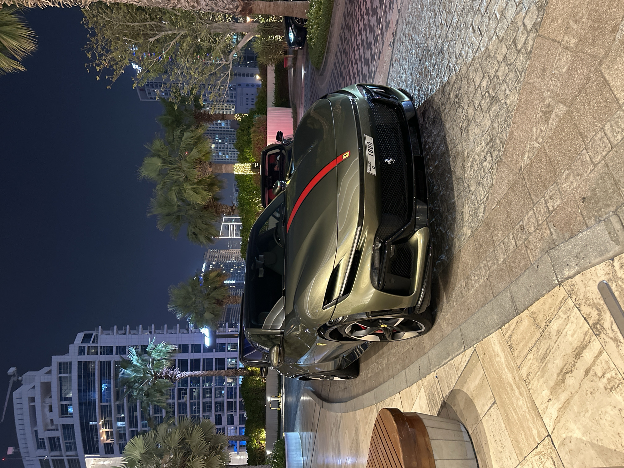 Olive green Ferrari Purosangue parked on Dubai cobblestones at night