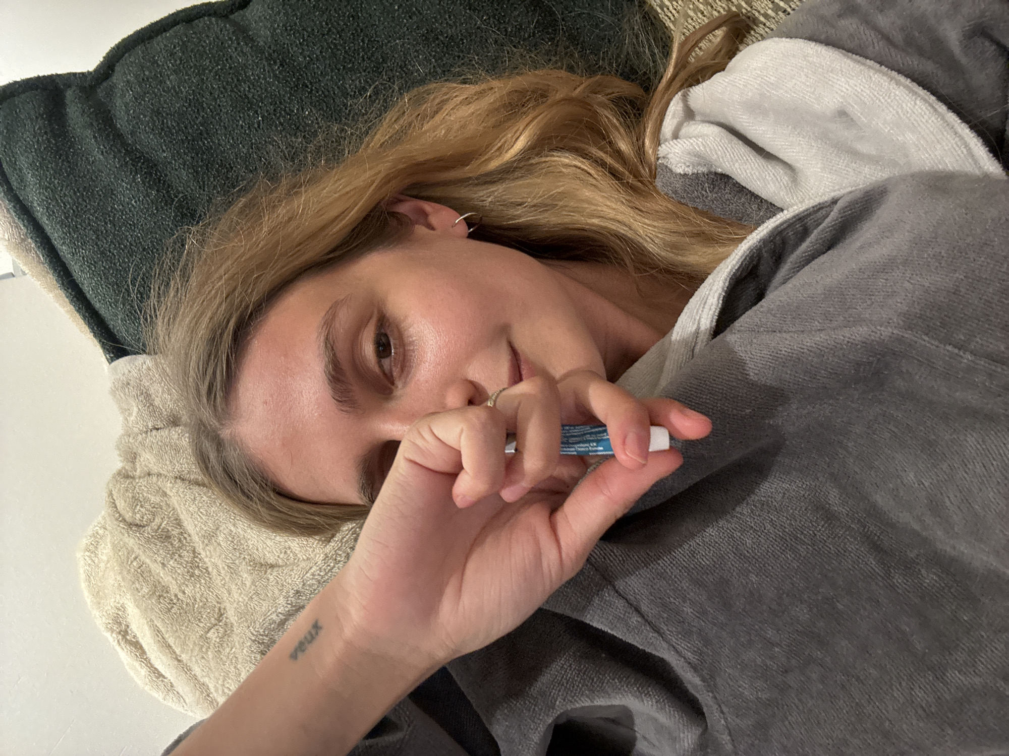 Person in grey robe rests on cushions holding tube