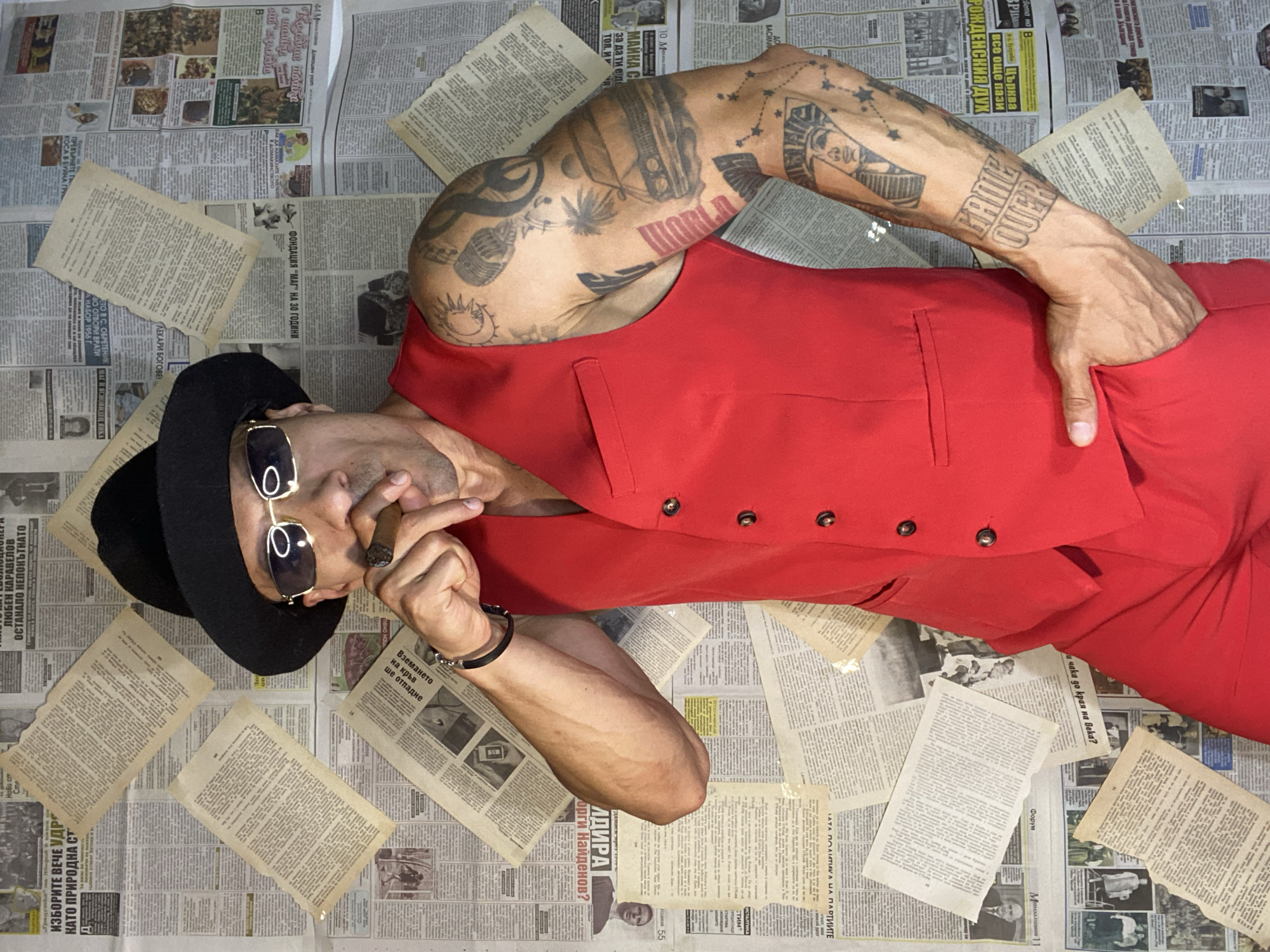 Dapper figure with cigar poses before newspaper-covered wall in Pleven