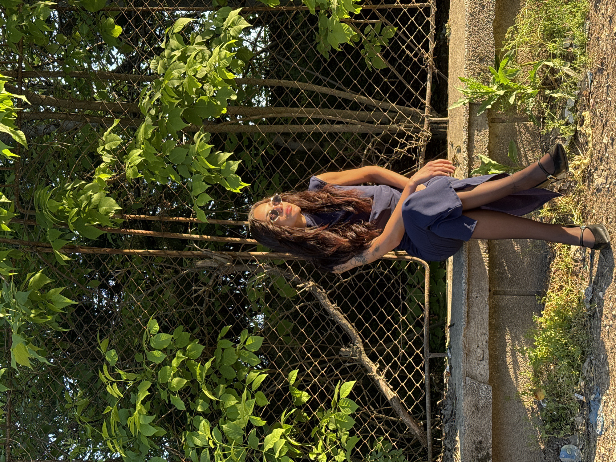 Woman rests on ledge near overgrown fence in Pleven