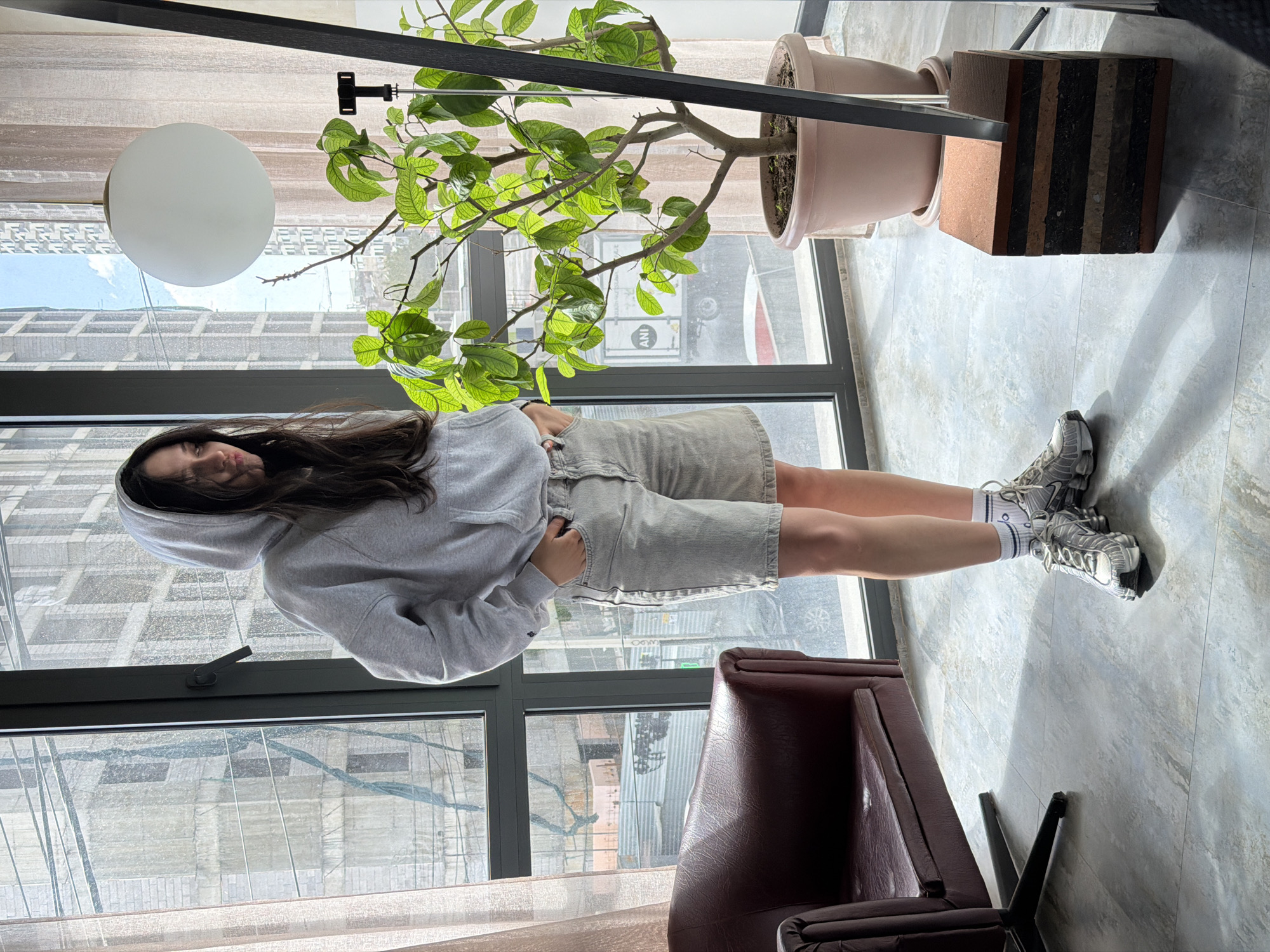 Woman in gray hoodie stands by window in Yerevan