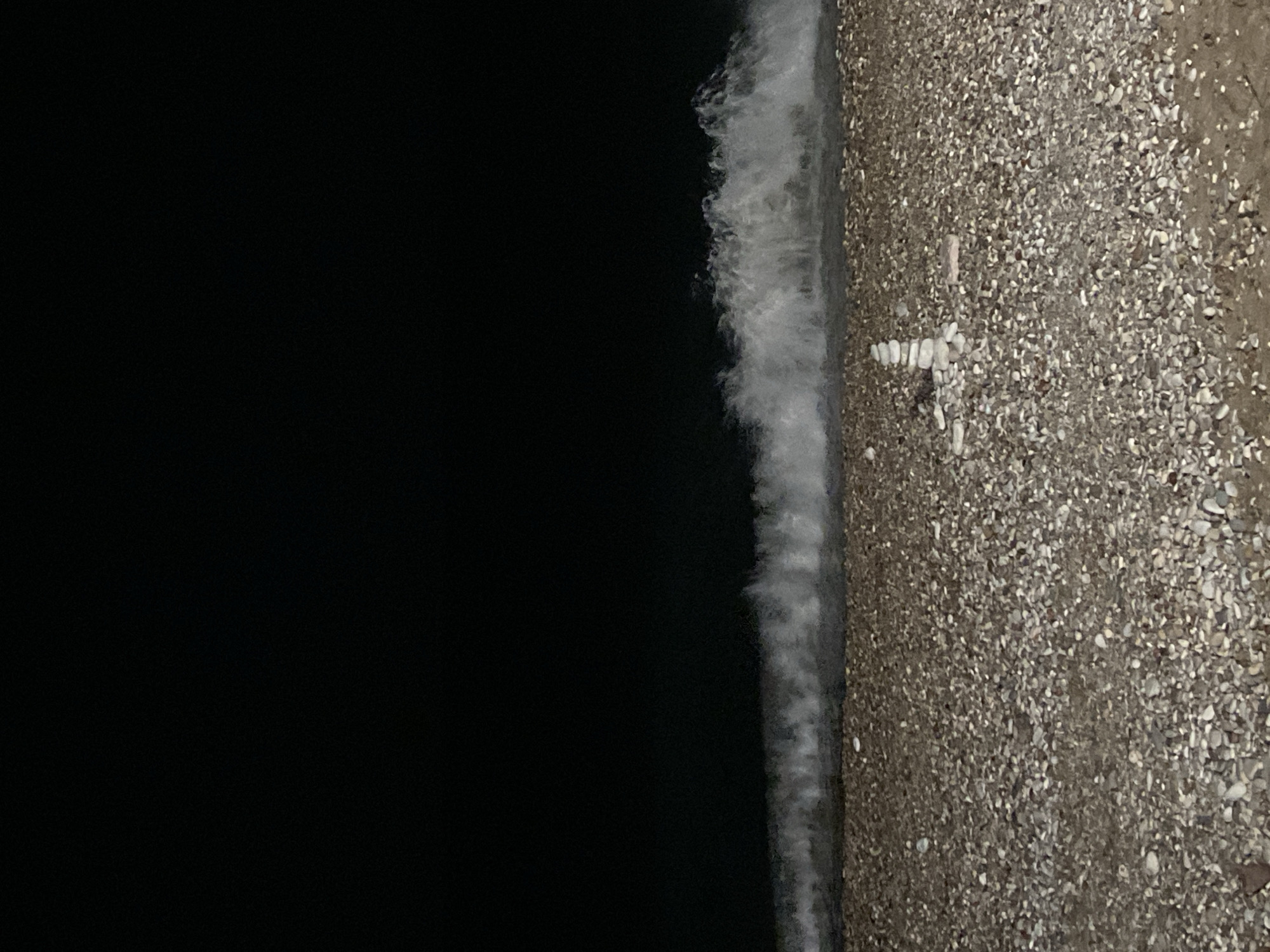 Nighttime waves wash pebble beach with stone cross in Bar