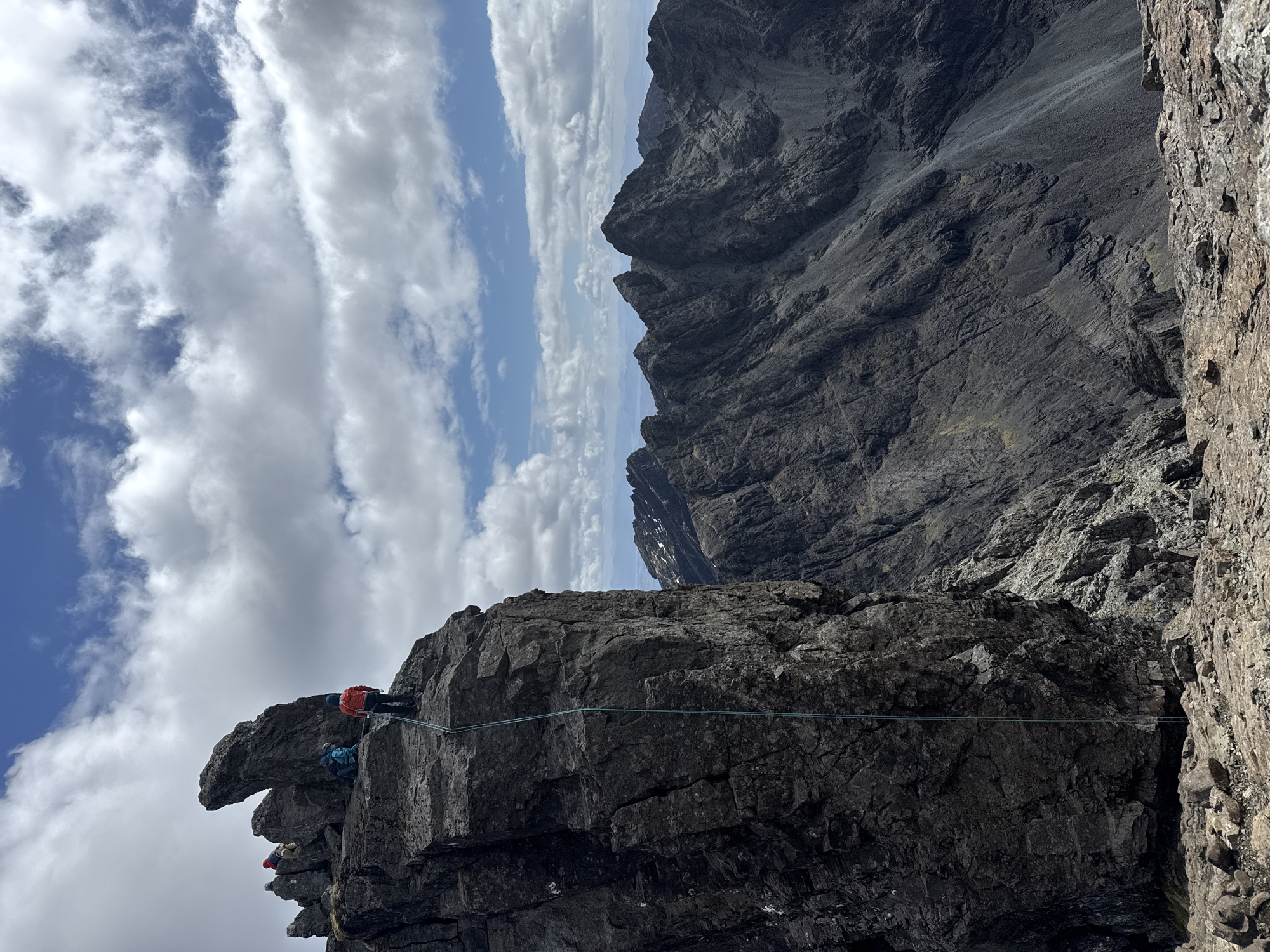 Three climbers scale jagged cliff in mountainous region