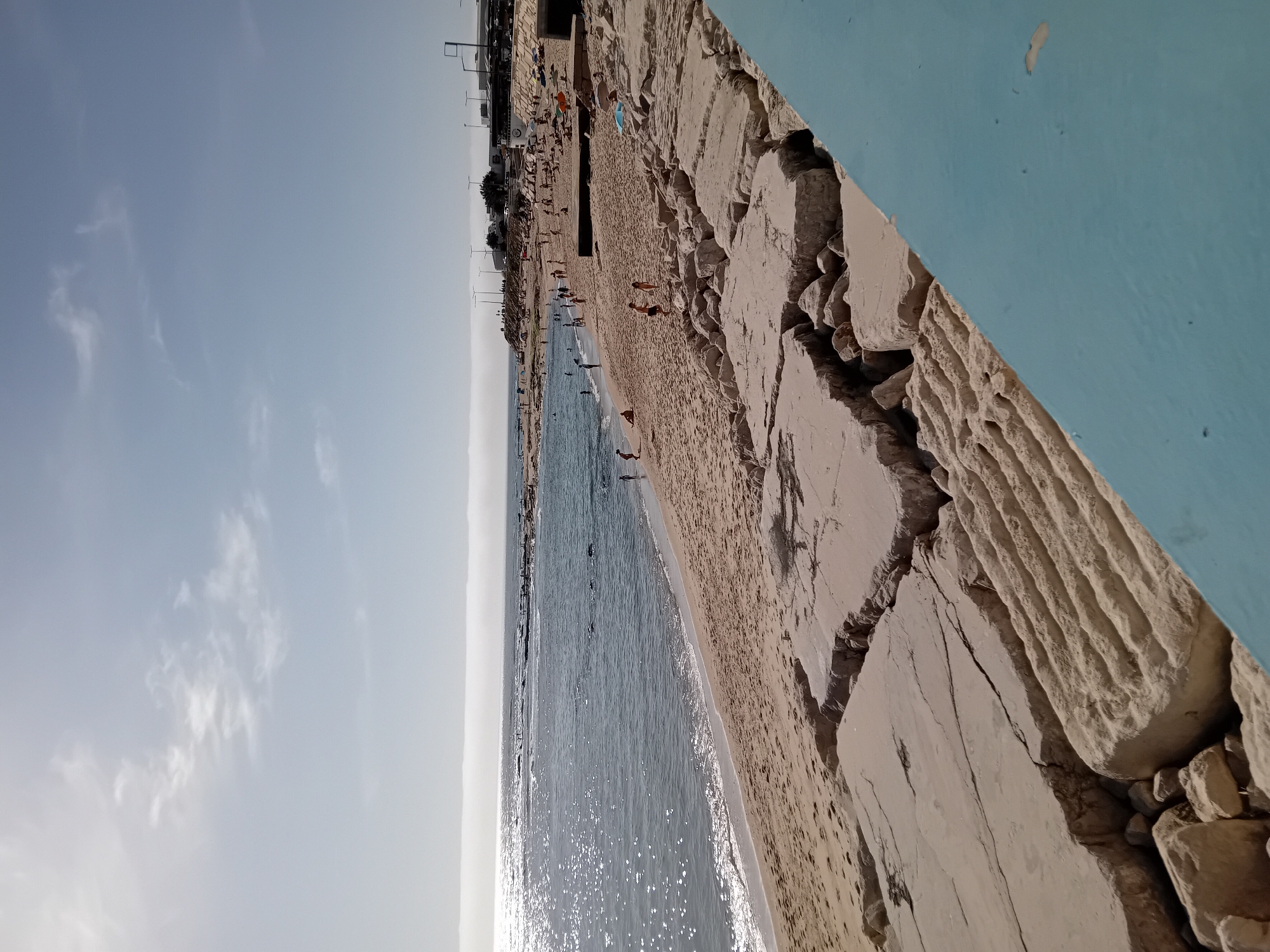 Beachgoers gather at coastal area with damaged concrete barrier