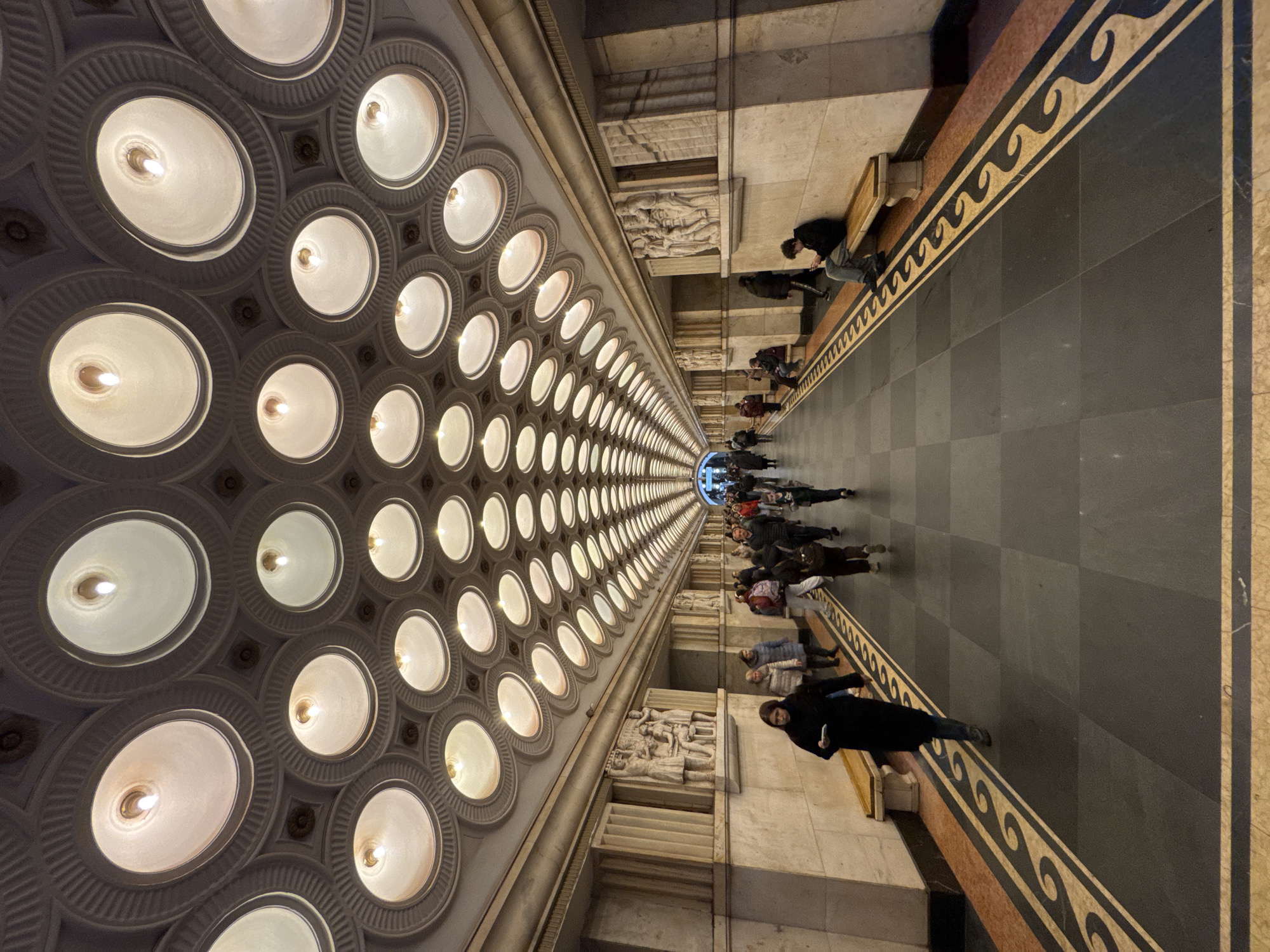 People walk through corridor with grid-pattern ceiling lighting