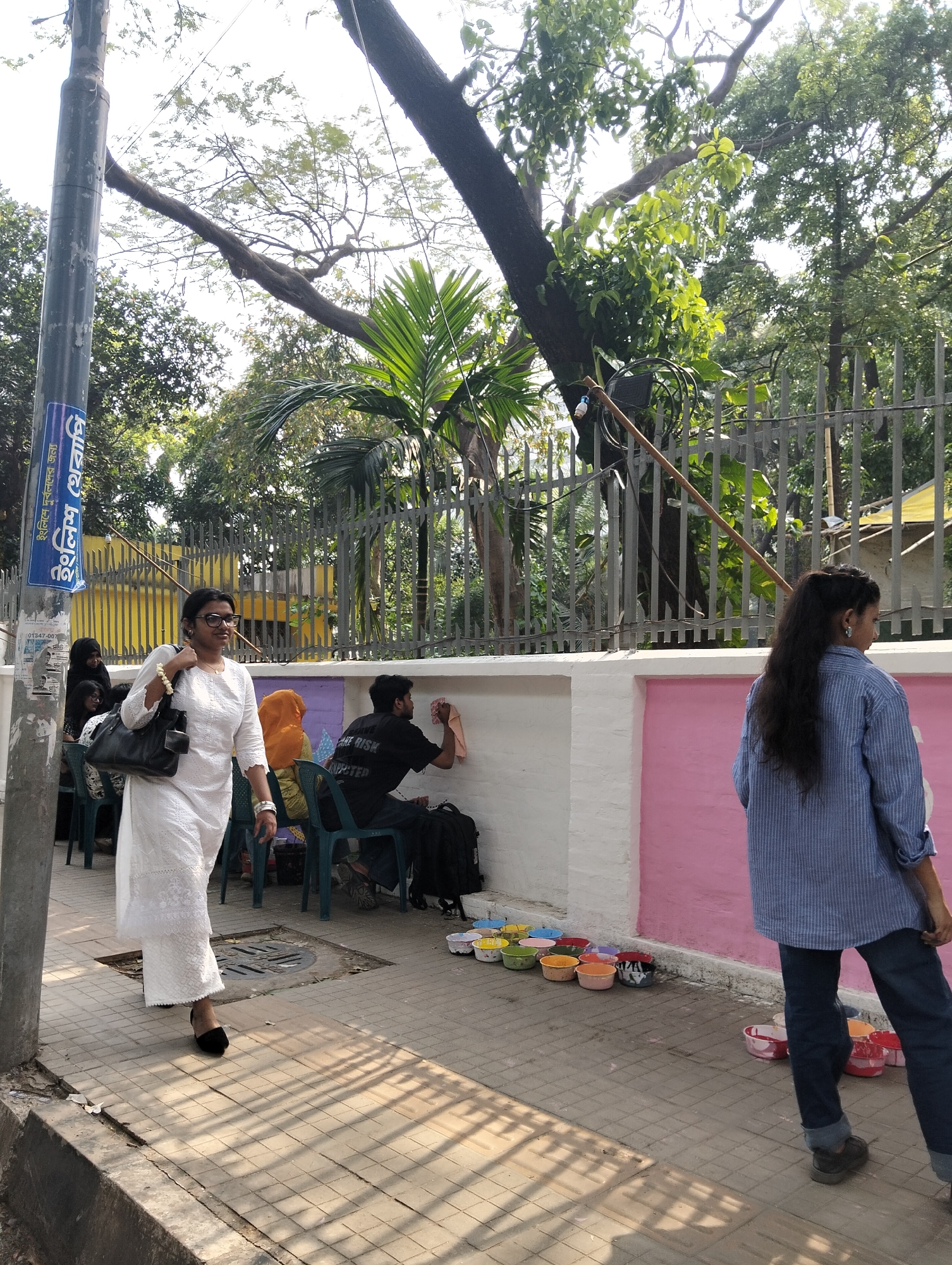 Pedestrians cross paths on Dhaka sidewalk during morning hours