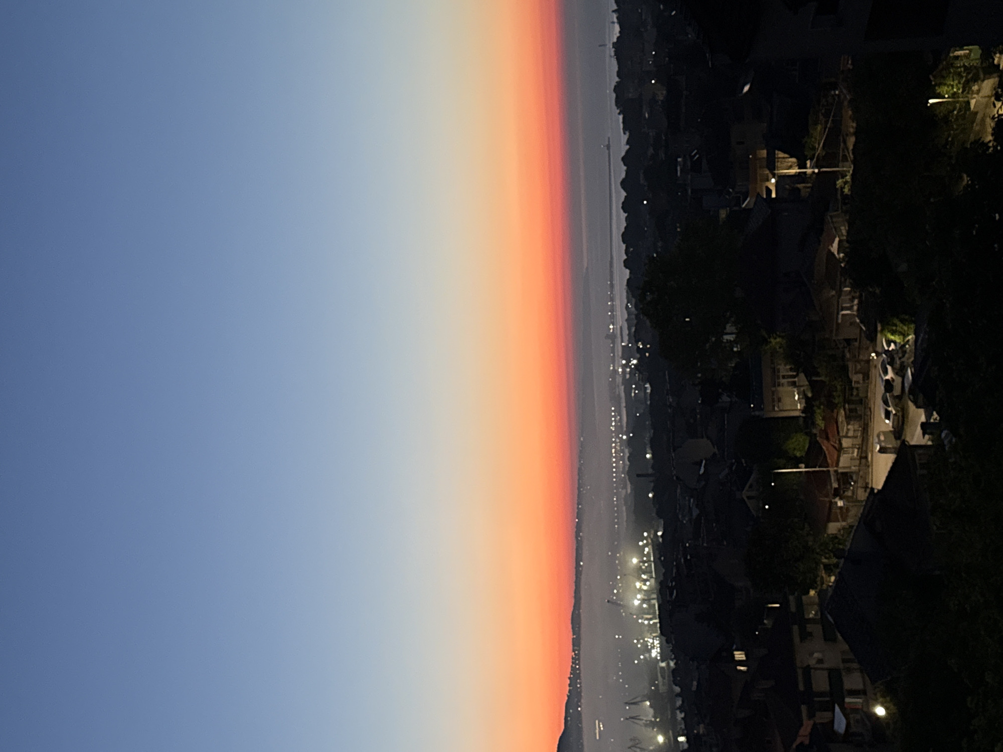 City skyline photographed during colorful twilight with crescent moon visible