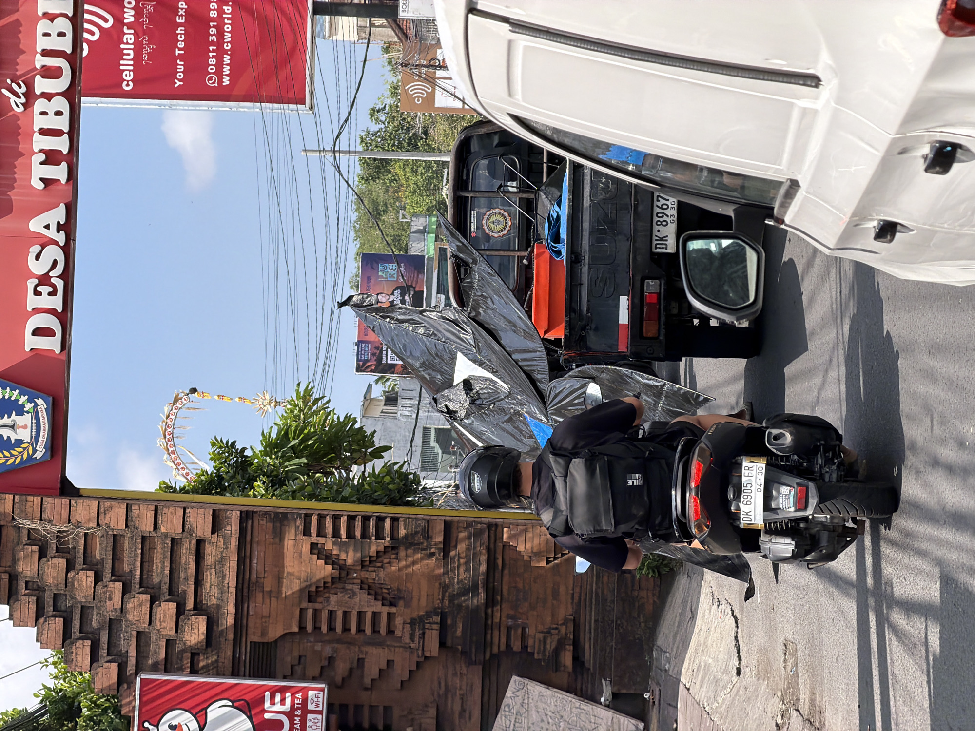 Scooter traffic rolls through a sunny North Kuta street