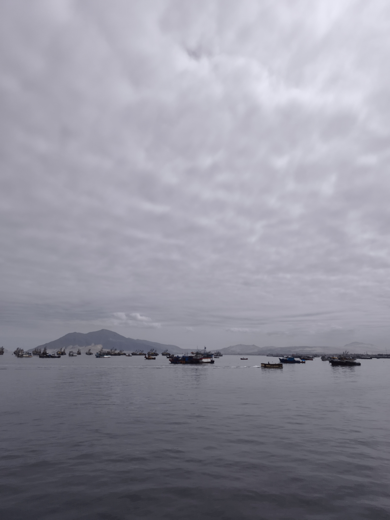 Fishing boats dot calm Chimbote harbor under overcast skies