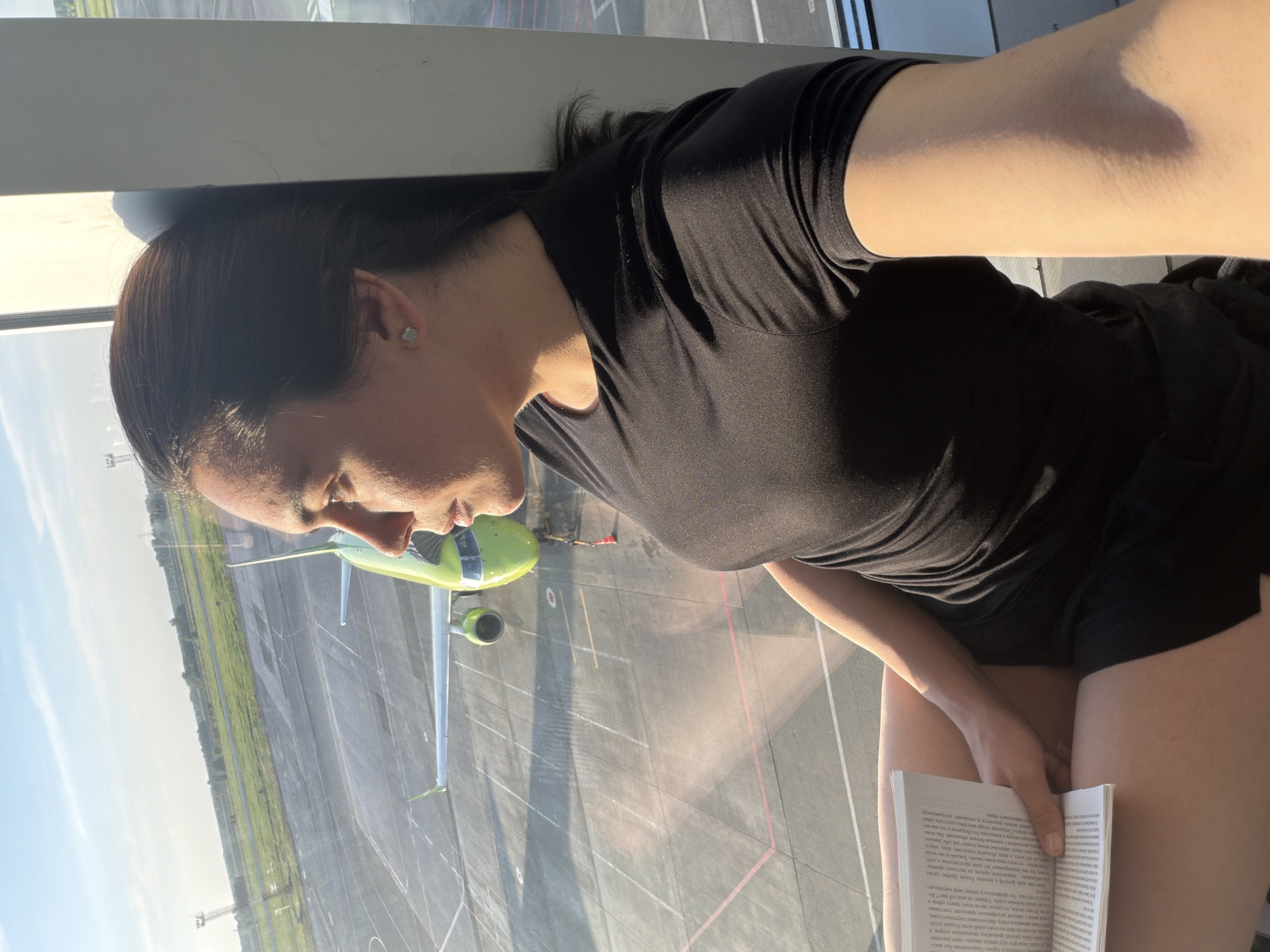 Woman reads book in airport lounge overlooking tarmac