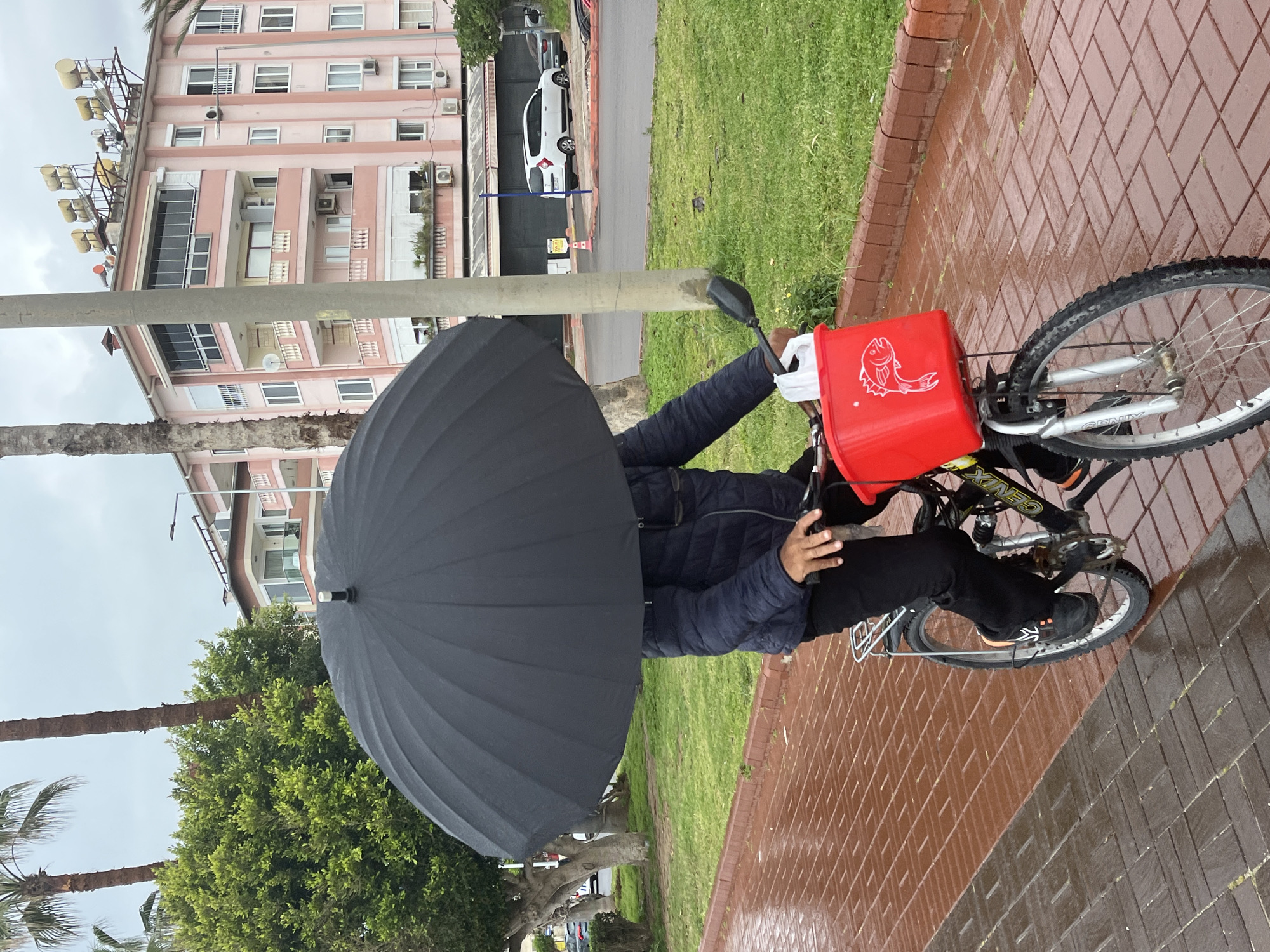 Cyclist rides with umbrella on wet sidewalk in Alanya