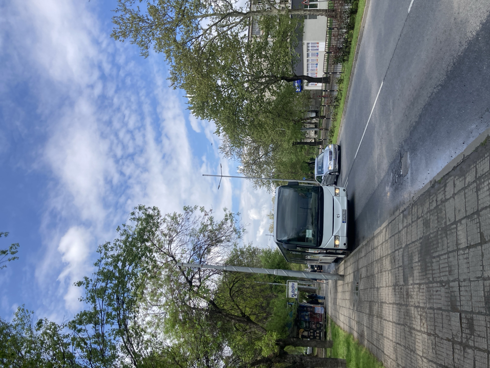 White bus parks on city street, car visible