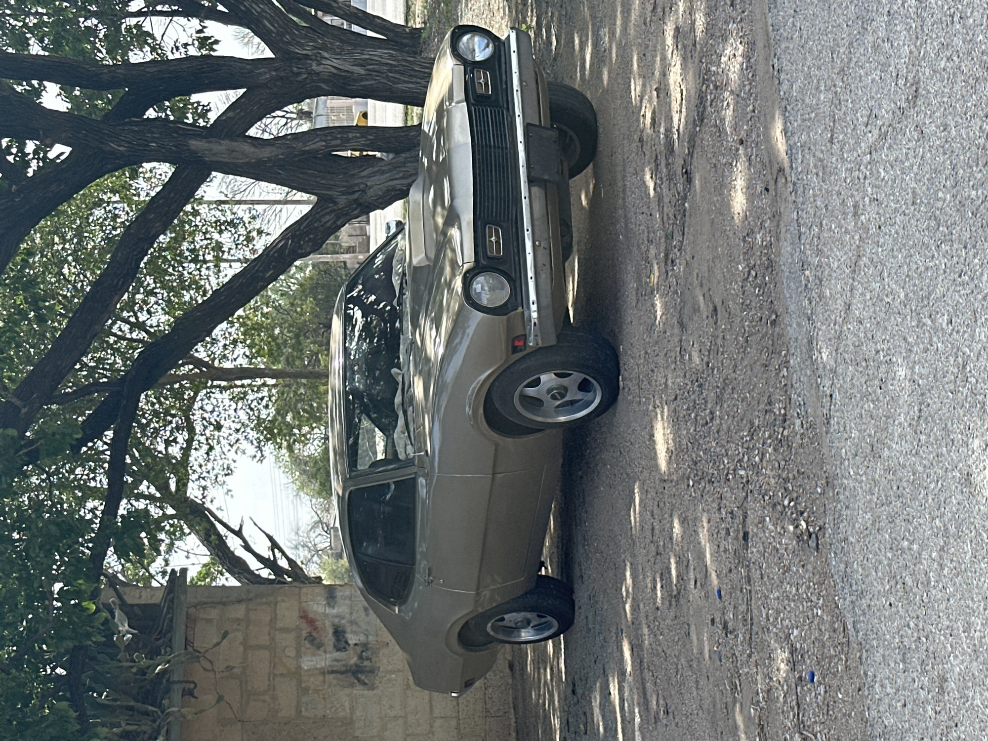Vintage gold Ford Maverick parked under trees in Venezuela