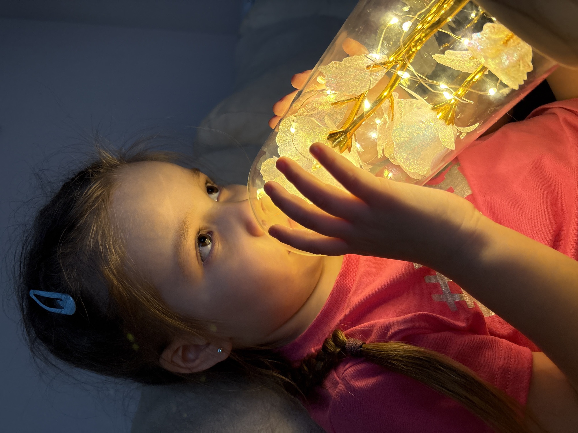 Girl plays with illuminated artificial flowers in glass container