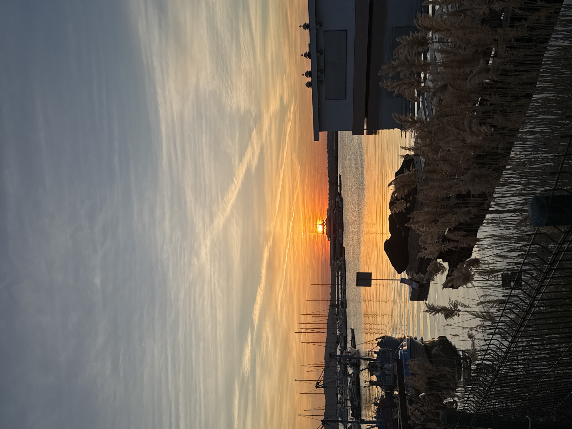 Sunset documented at Sozopol harbor with boats and contrails