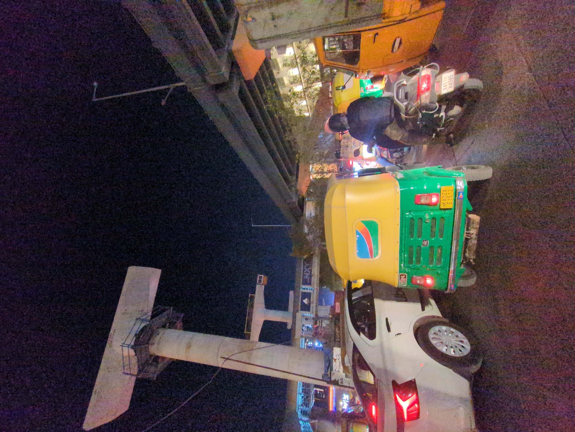 Auto-rickshaw parks beside white car on busy Bengaluru street