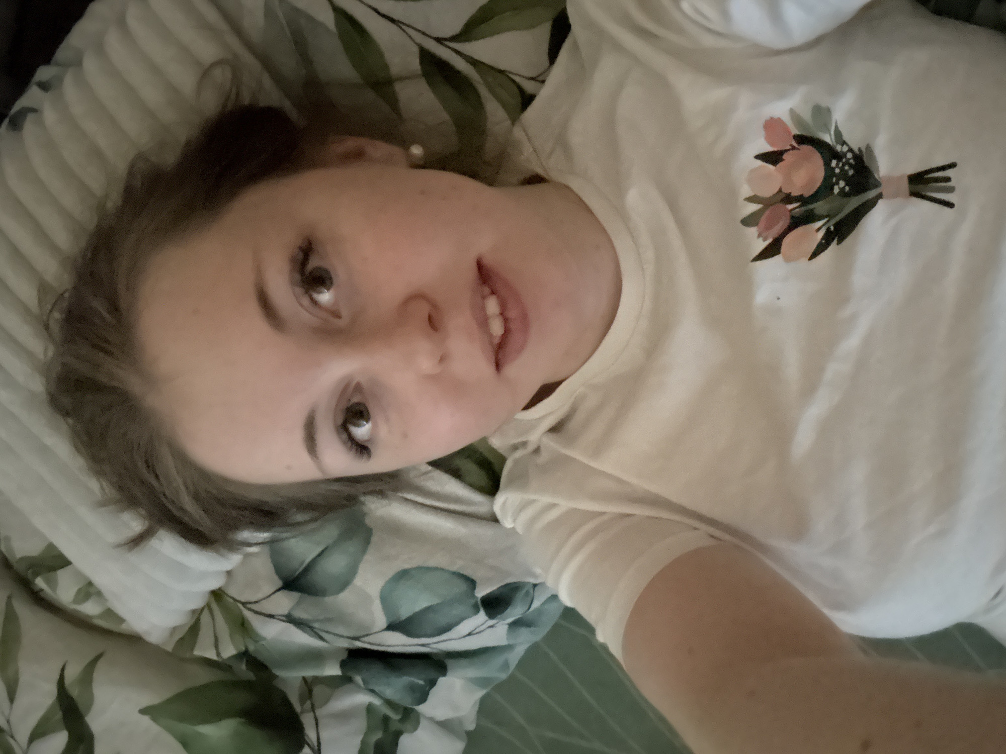 Woman rests on patterned bed in white floral shirt