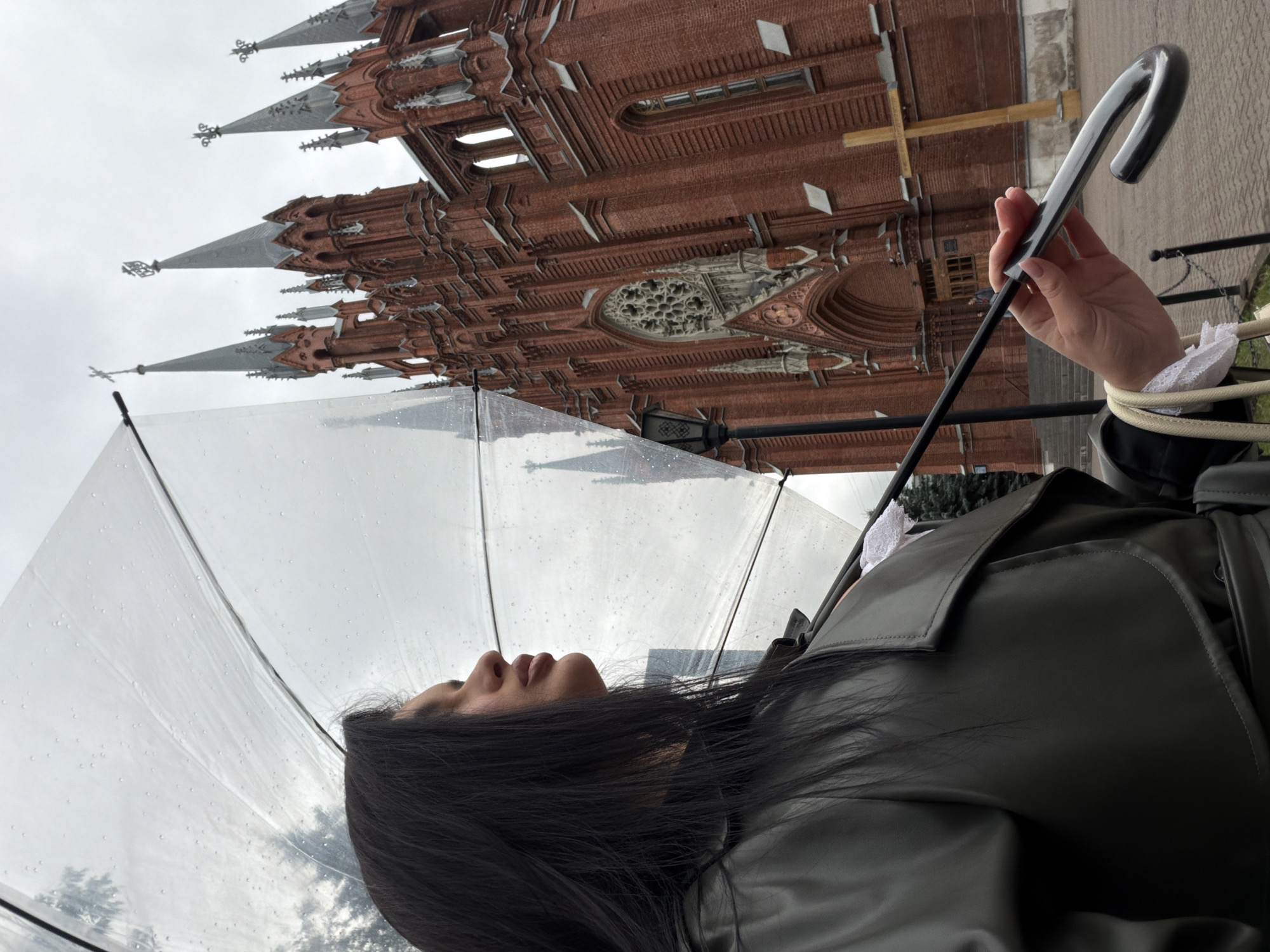 Clear umbrella in hand outside Moscow's Gothic red brick architecture