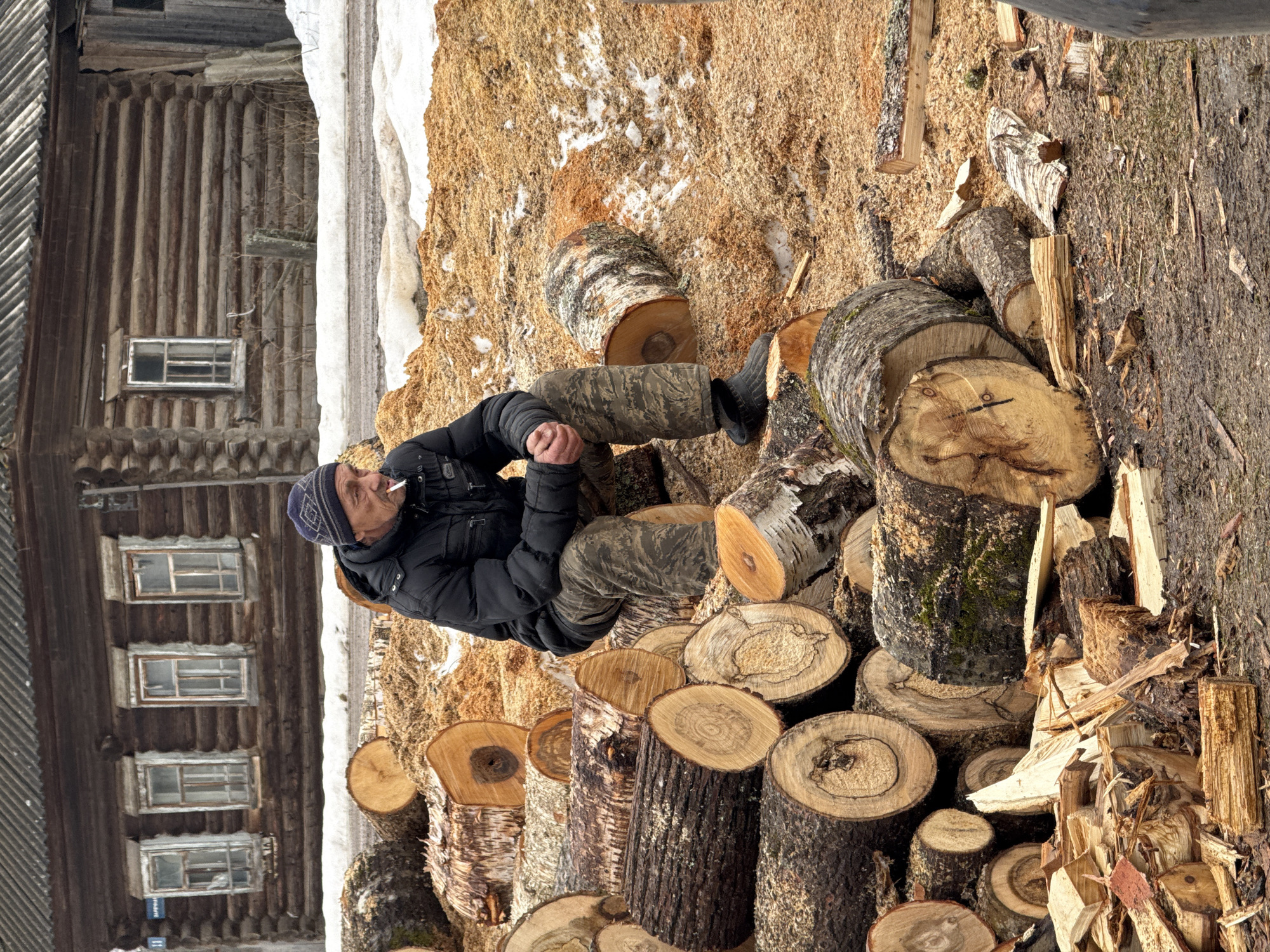 Family gathered around log pile in rural Russian village