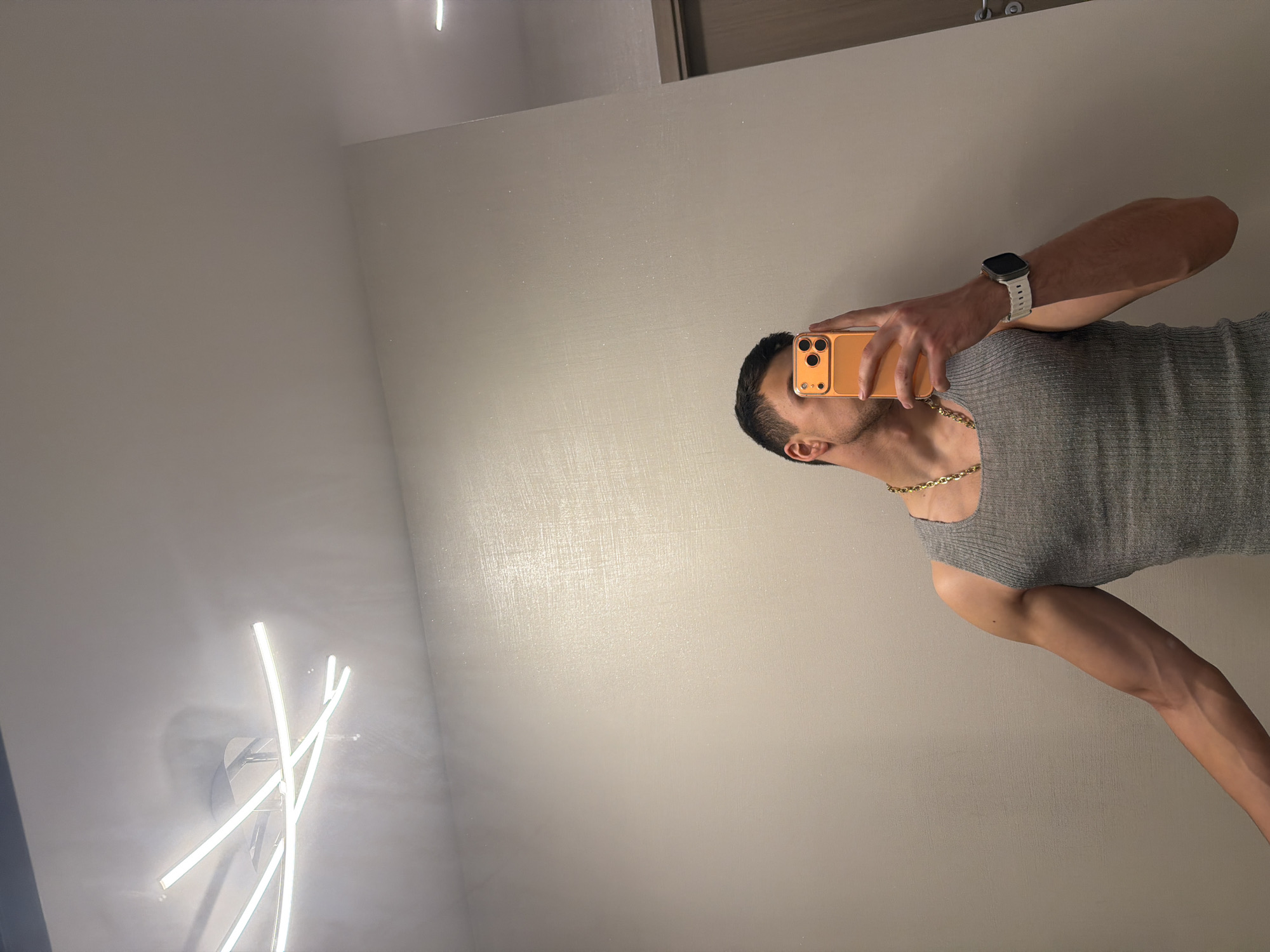 Man takes mirror selfies indoors with orange smartphone