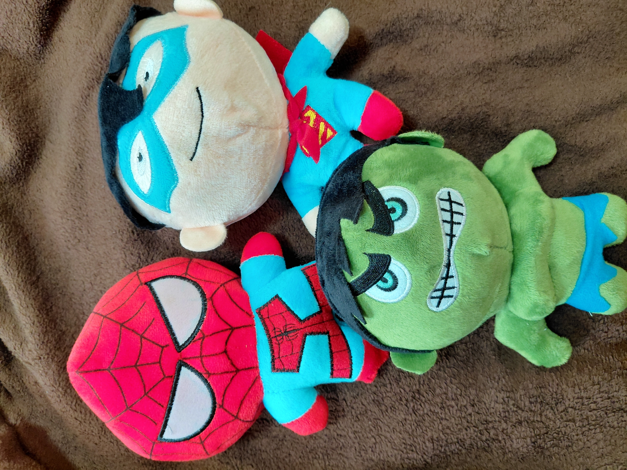 Three superhero plush toys spotted on brown surface