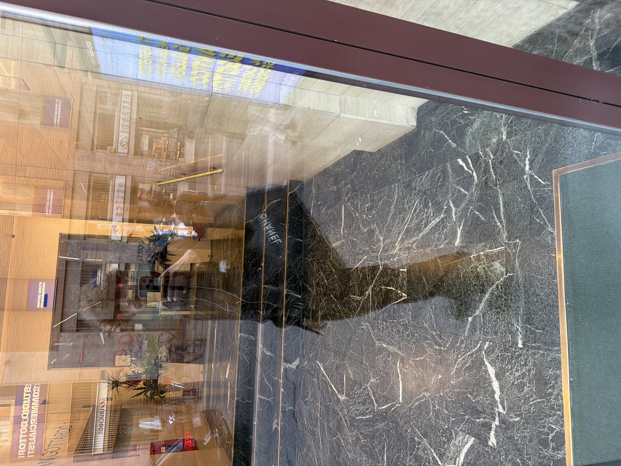 Window reflection captures Milan street scene with Italian storefronts