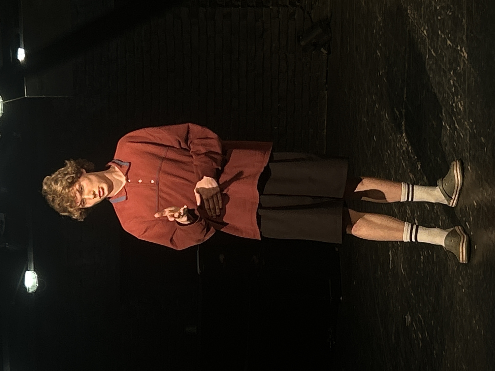 Young performer rehearses on dimly lit stage, captured by witnesses