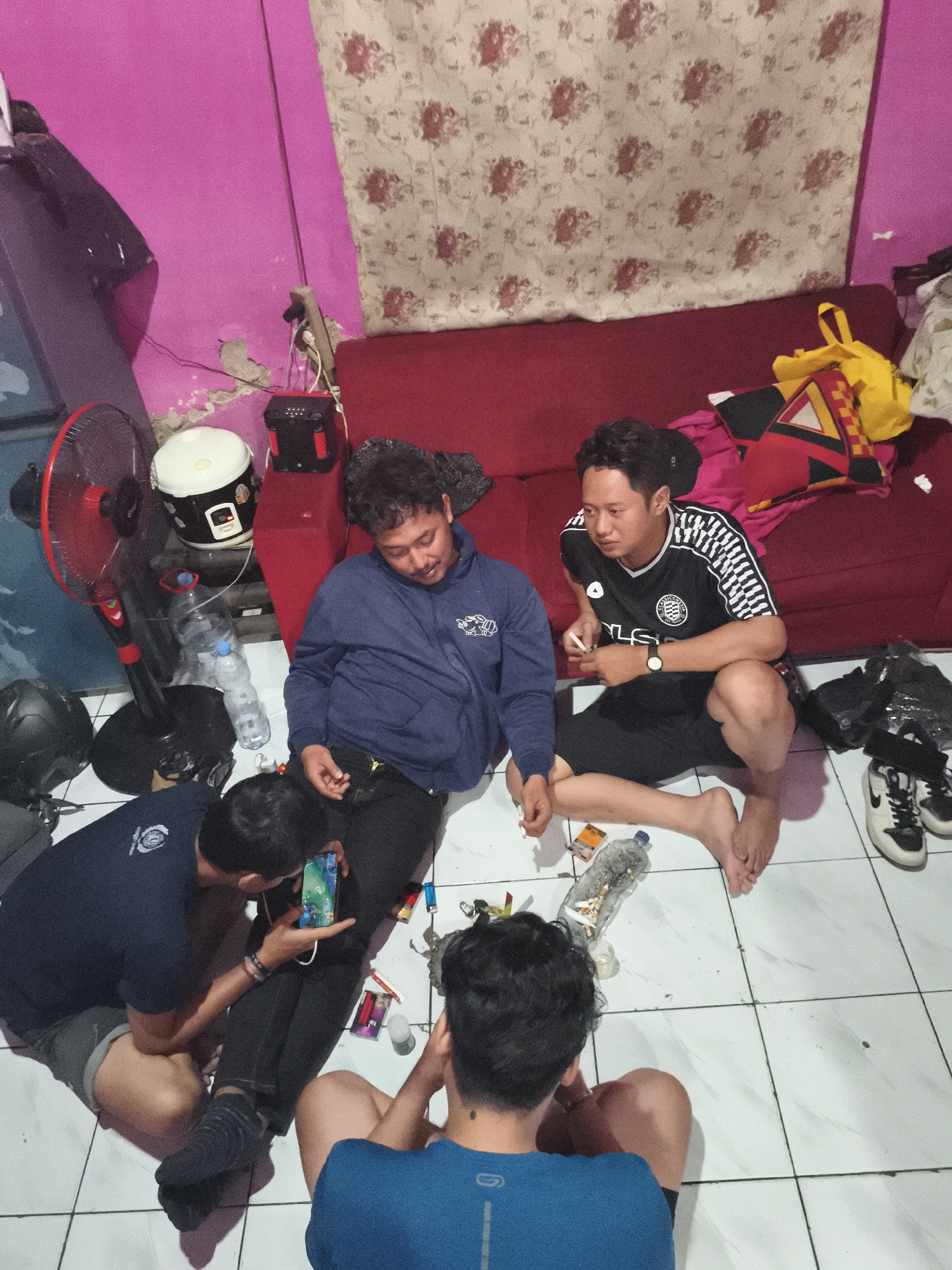 Young men gather on floor using phones in Depok room