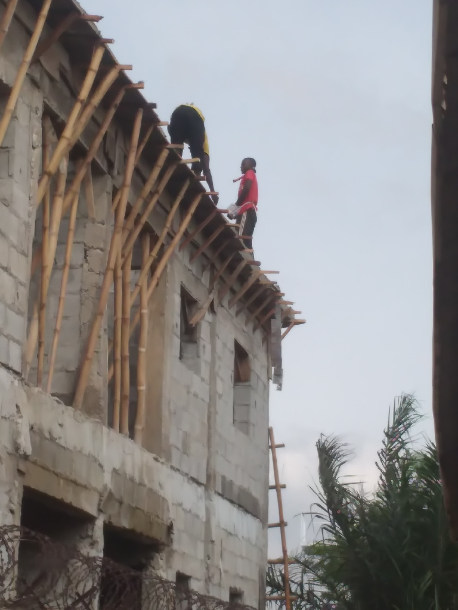 Concrete block building mid-construction, workers active on scaffolding and roof