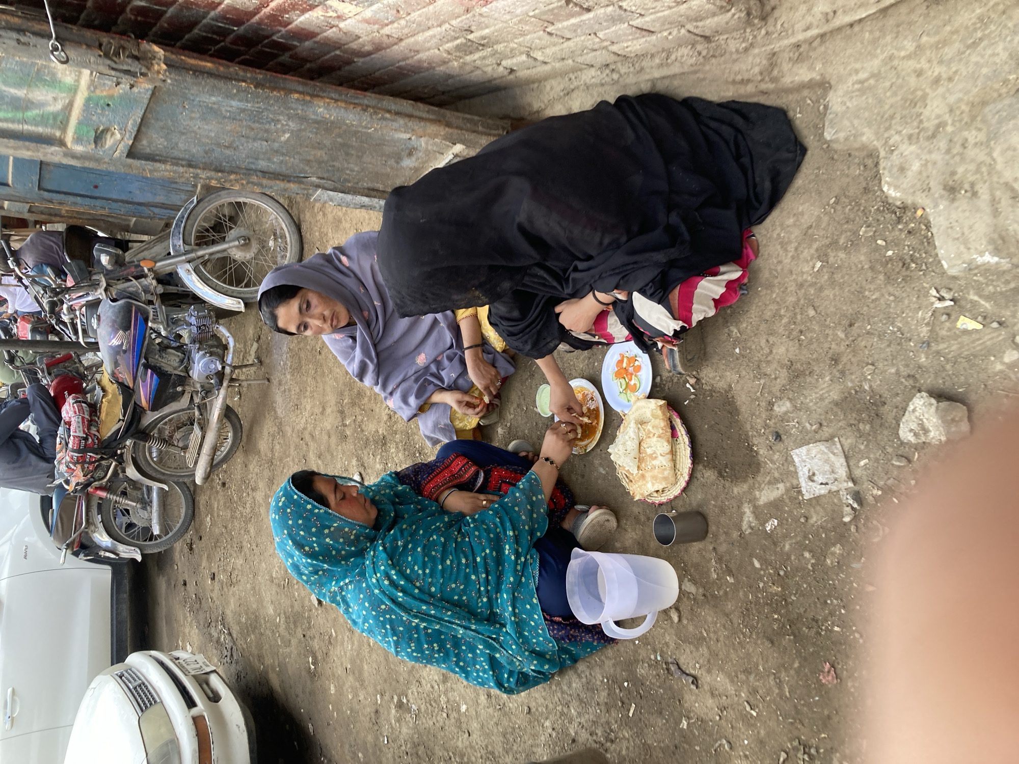 Three women share outdoor meal in Quetta alleyway