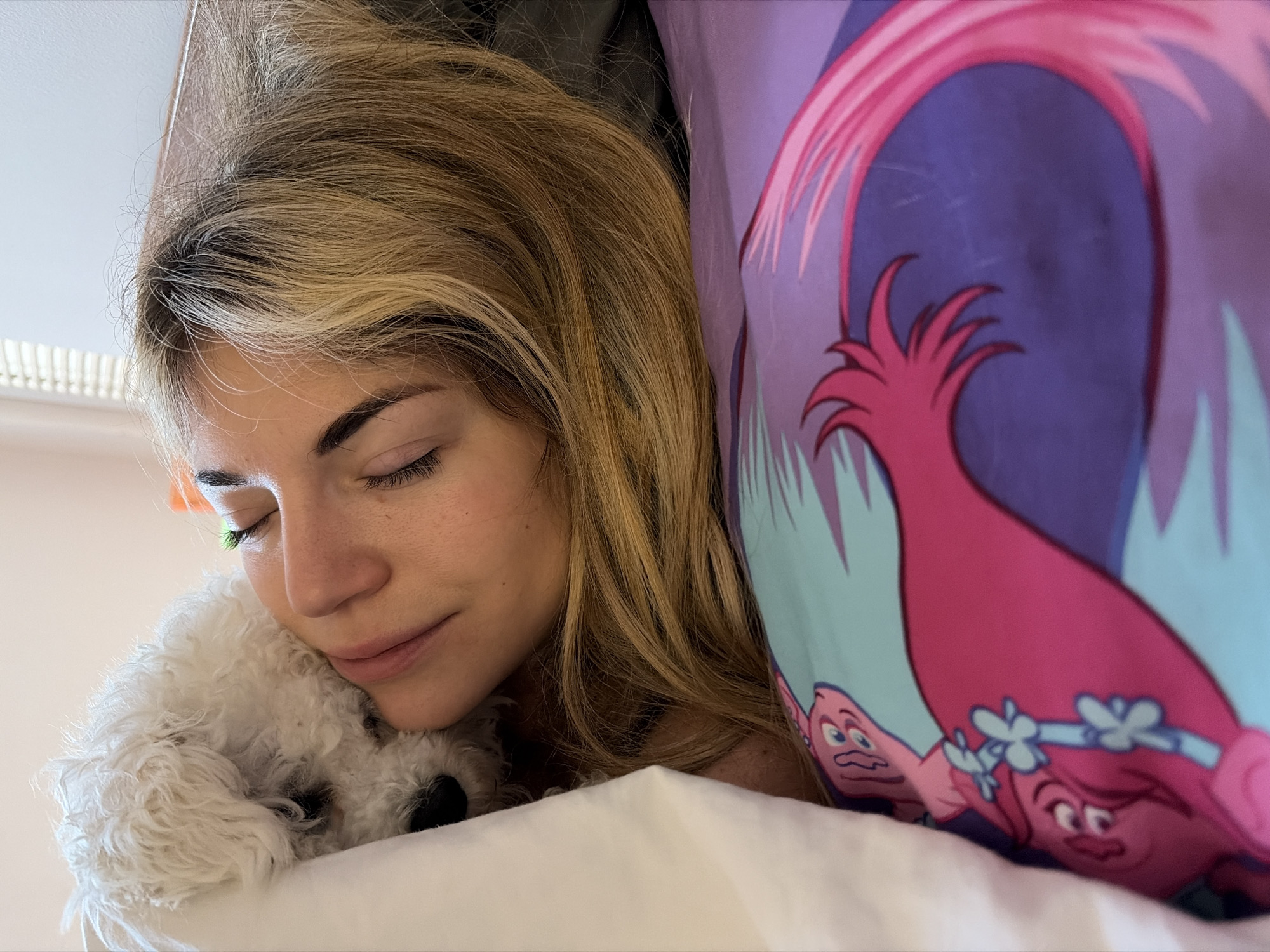 Woman rests peacefully in bed with white Bichon Frise