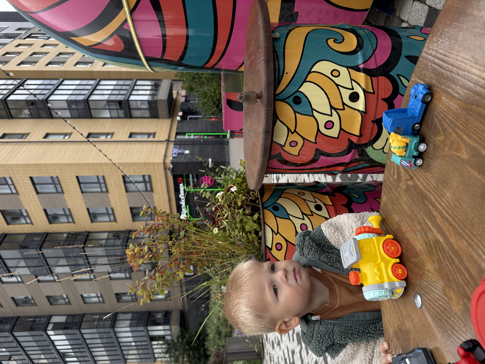Toddler lunch break at a colorful food truck, sparrows included