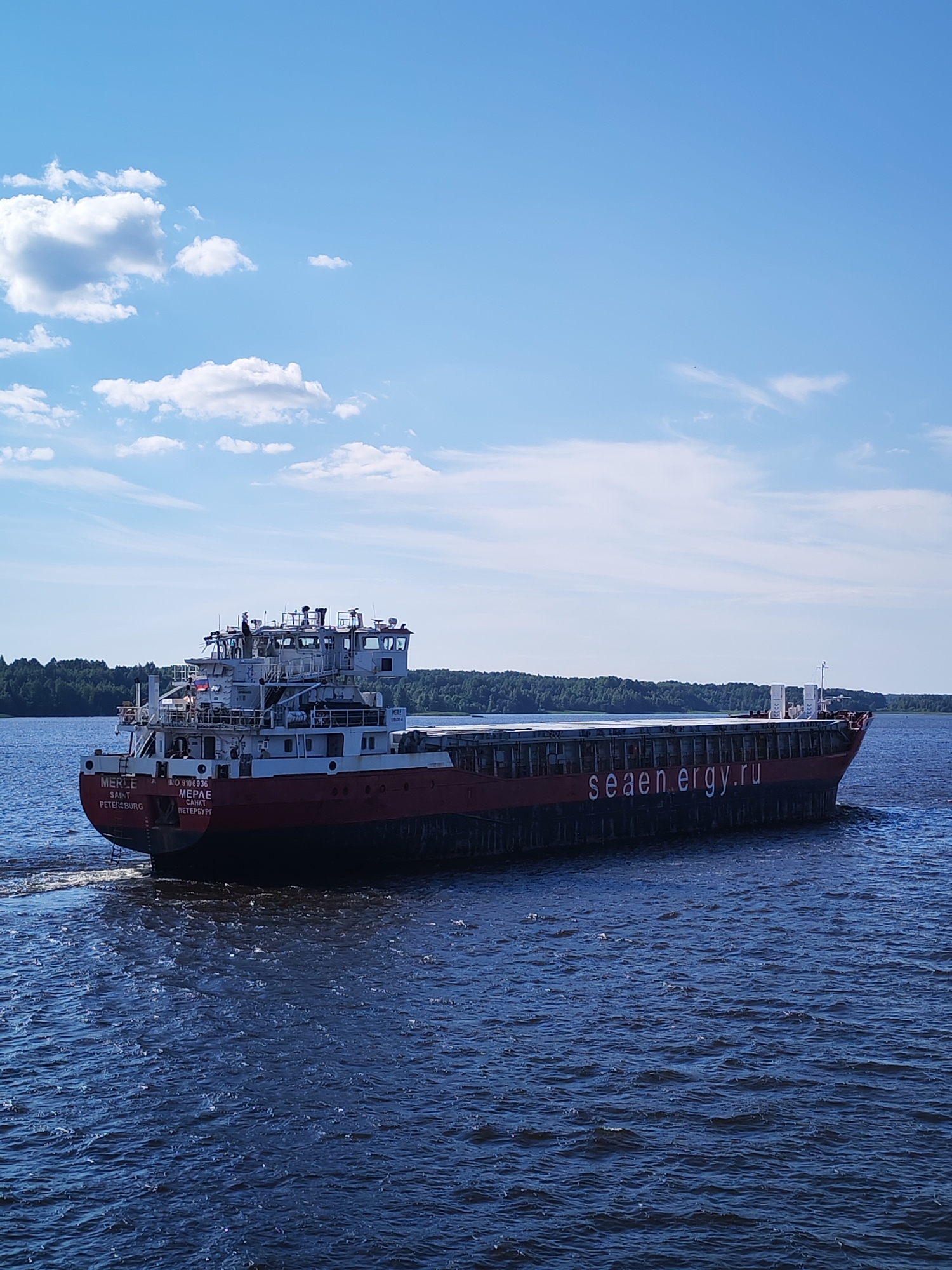 Red-hulled cargo ship MERLE sailing Russian river on clear day