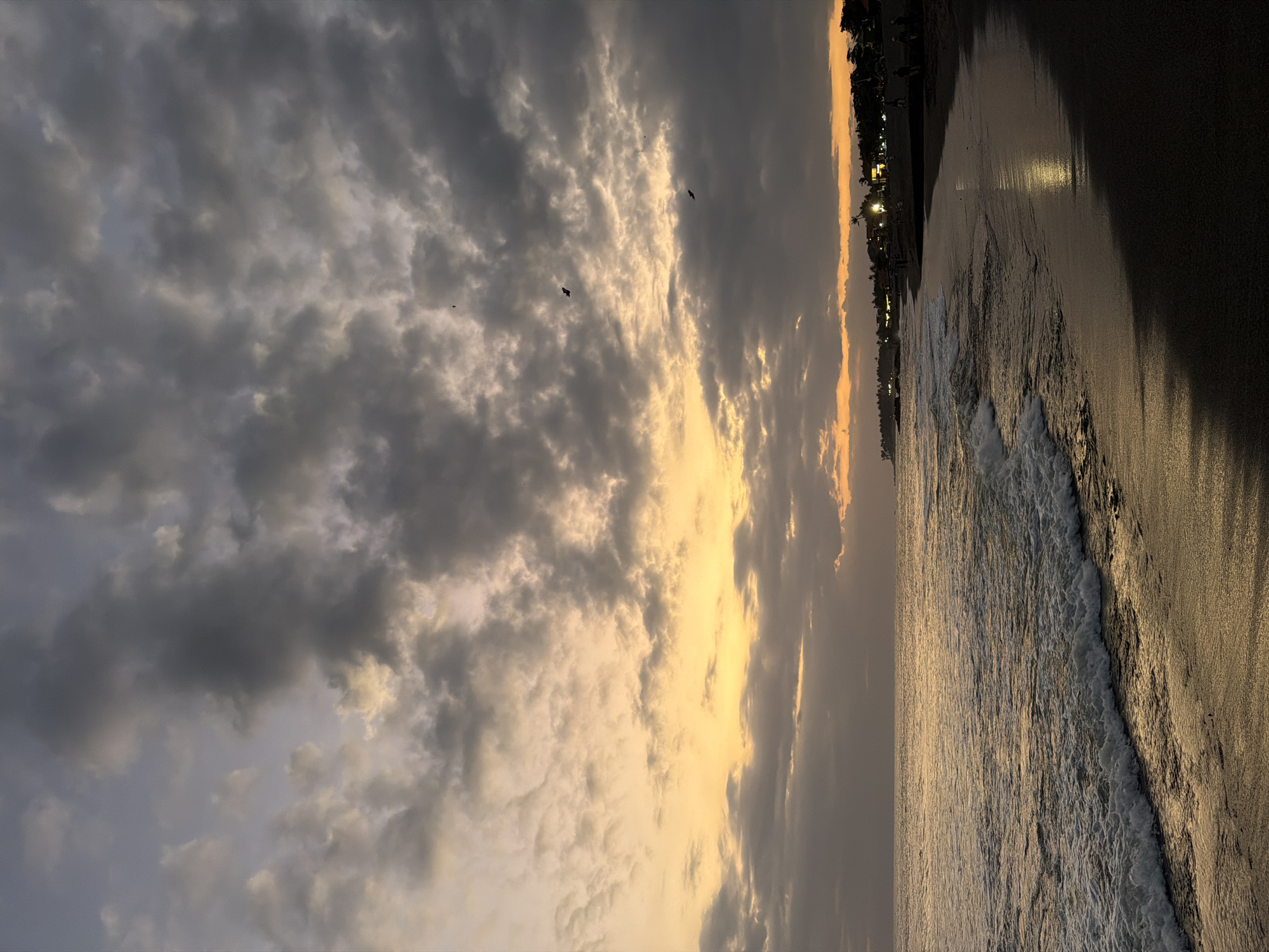 Sunset on a dark sand Bali beach, couples and coastline