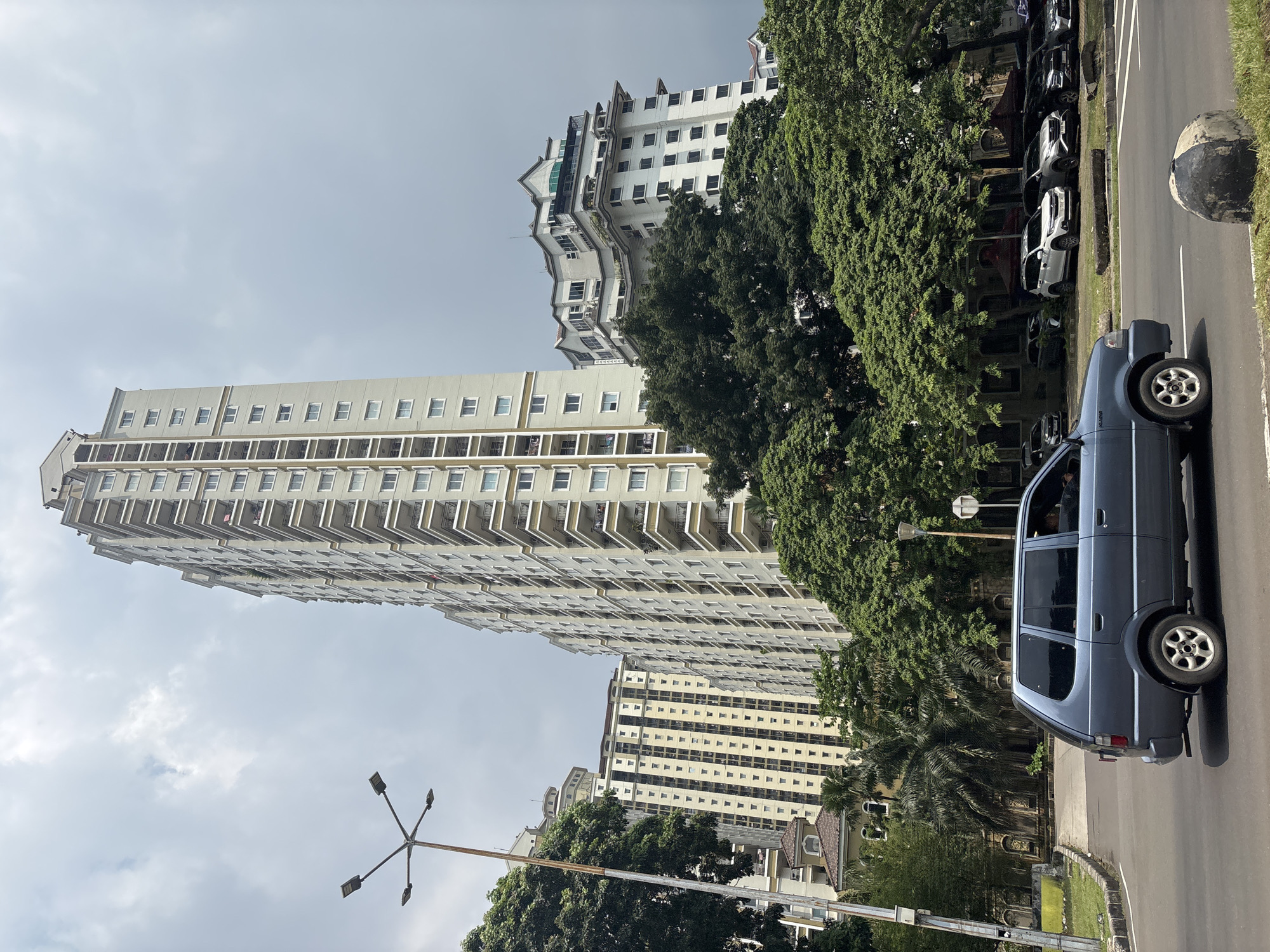Blue car parked among vehicles on tree-lined Jakarta street