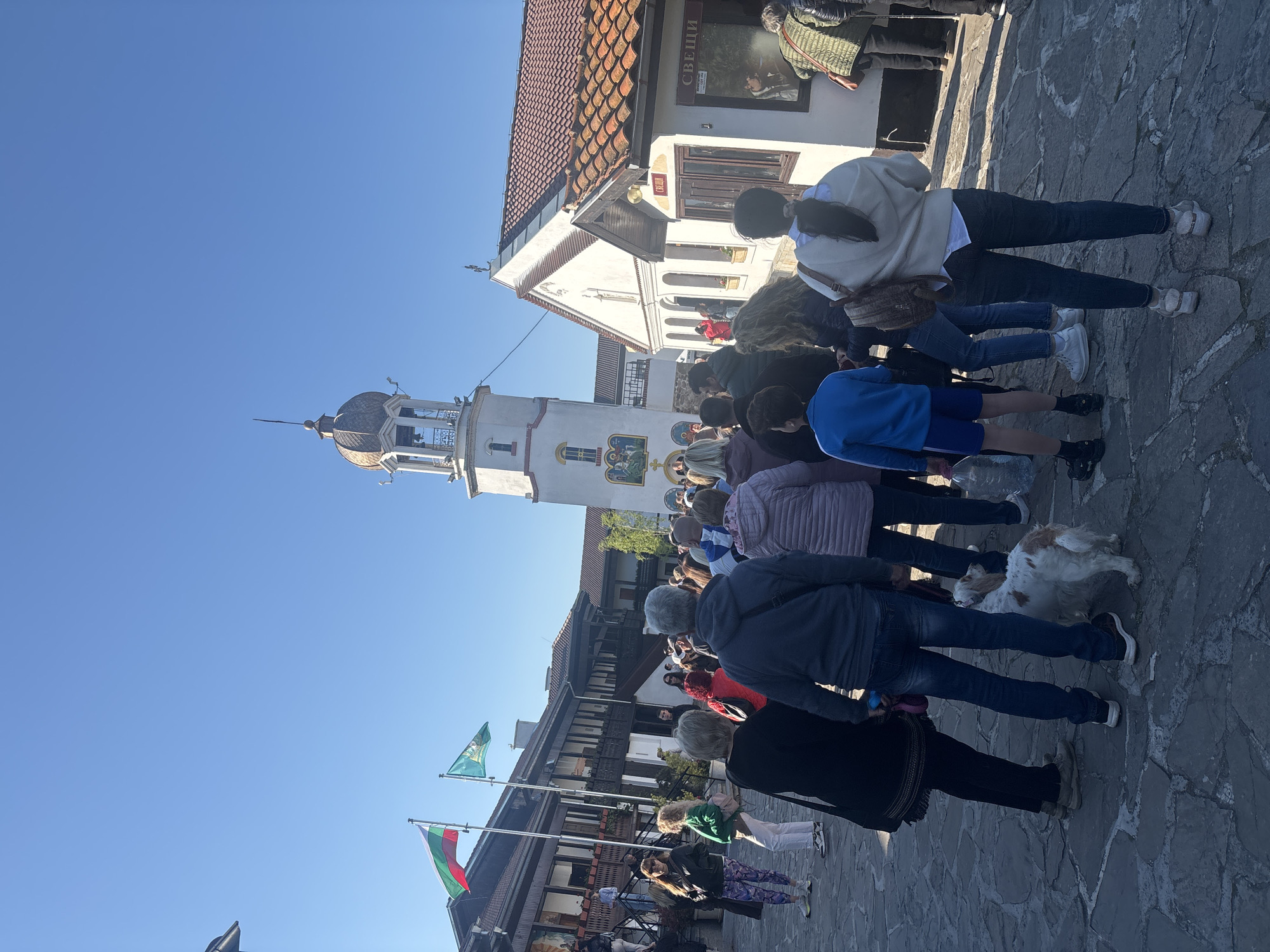 People gather around white bell tower in Pomorie square