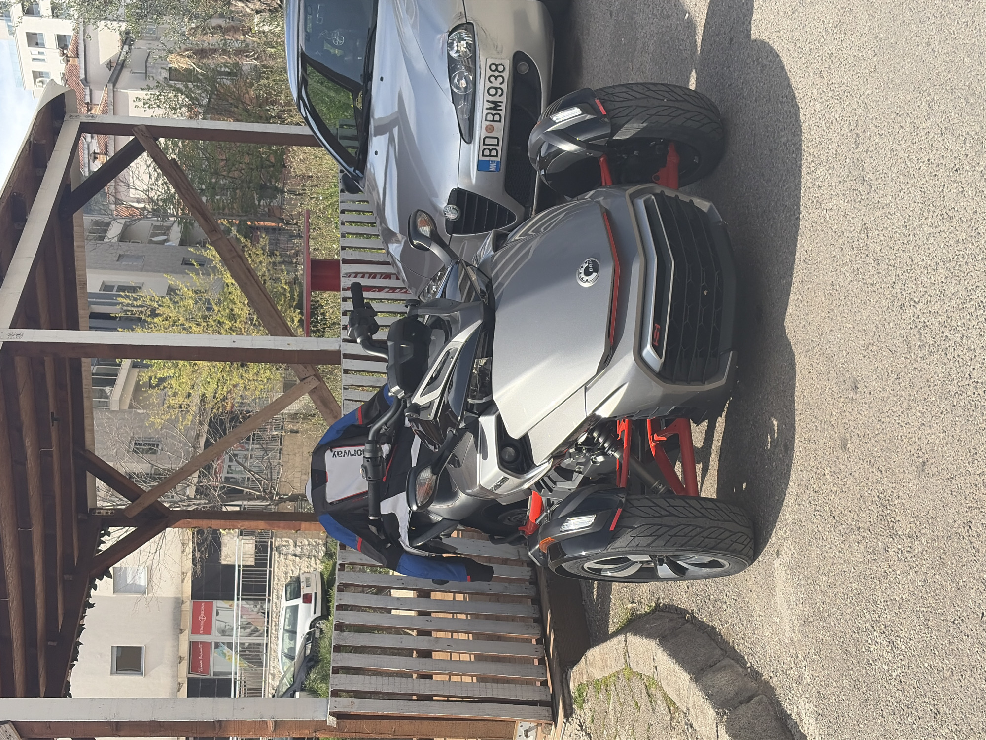 Can-Am Spyder parked with silver car near covered structure