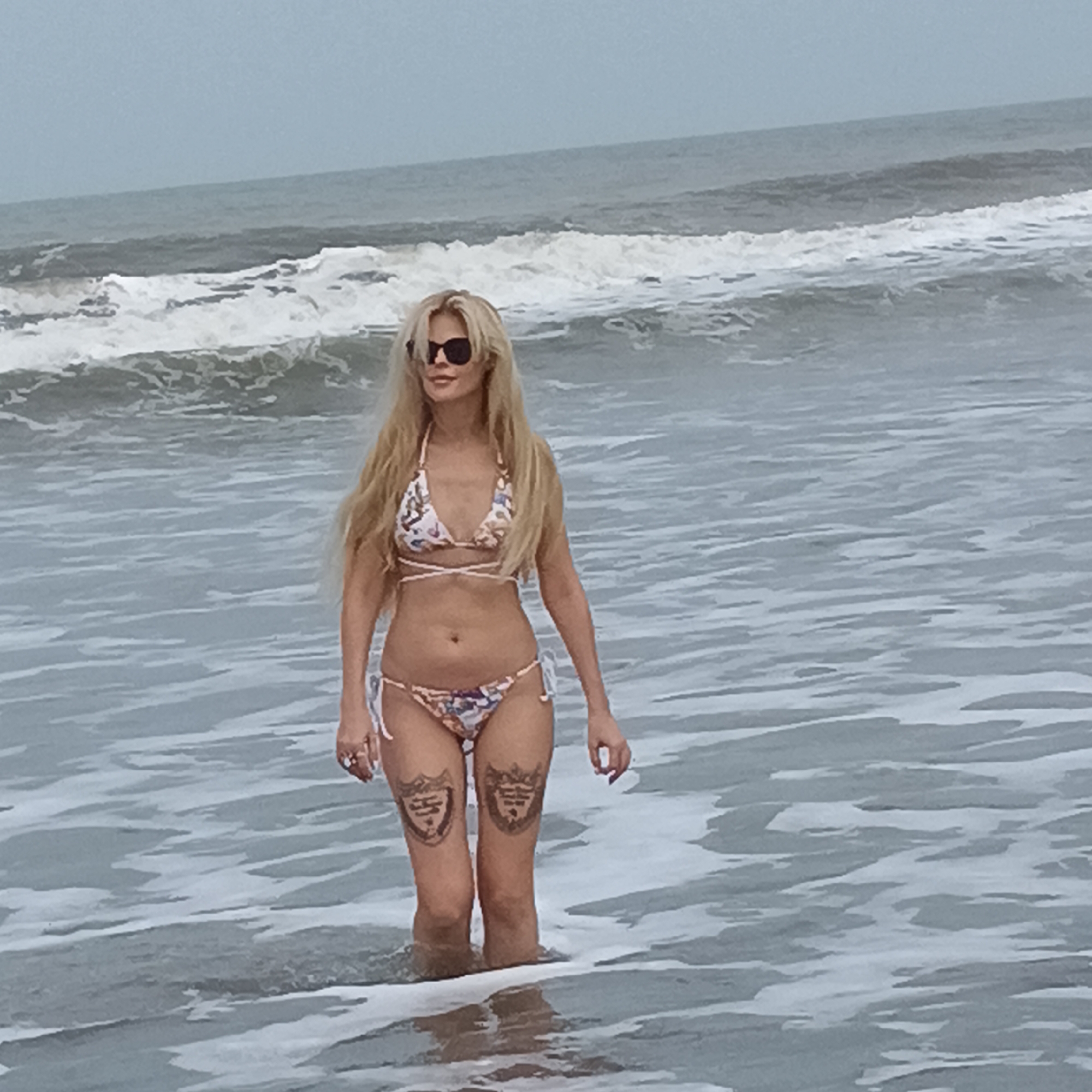 Woman stands in ocean waves under overcast morning sky