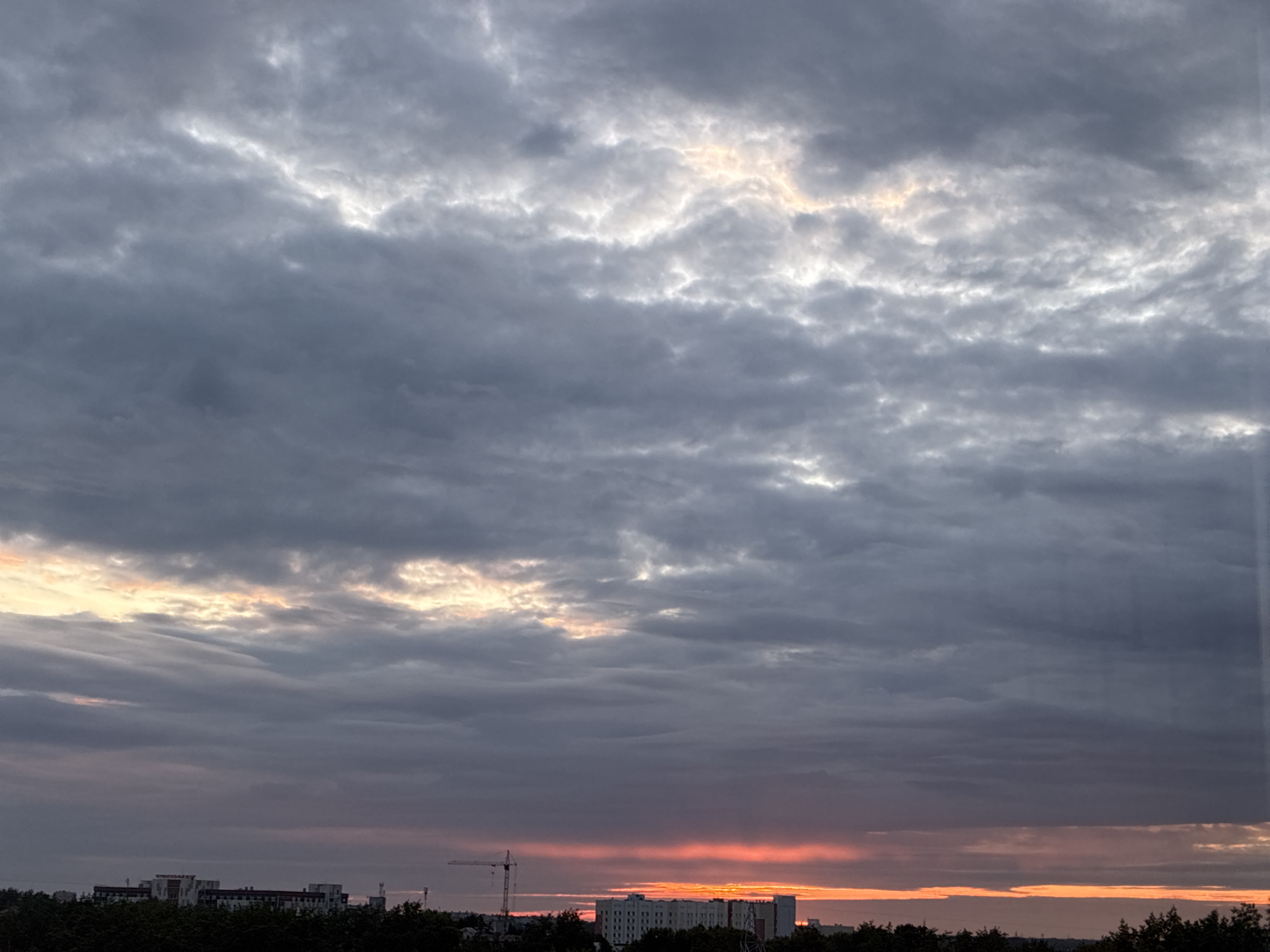 Dramatic sunset documented over city skyline through heavy clouds