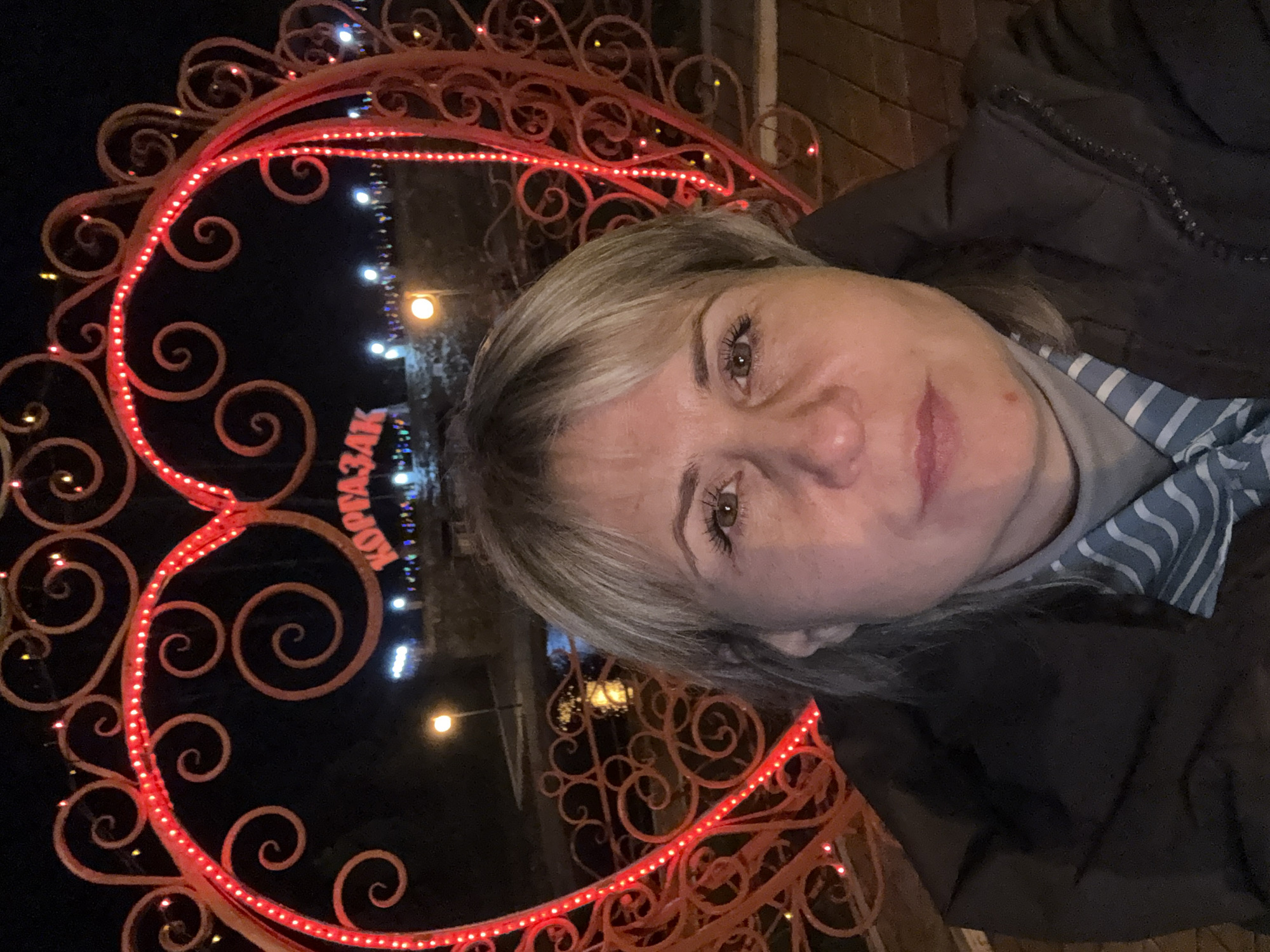 Woman stands by illuminated heart structure in Komsomol nighttime display