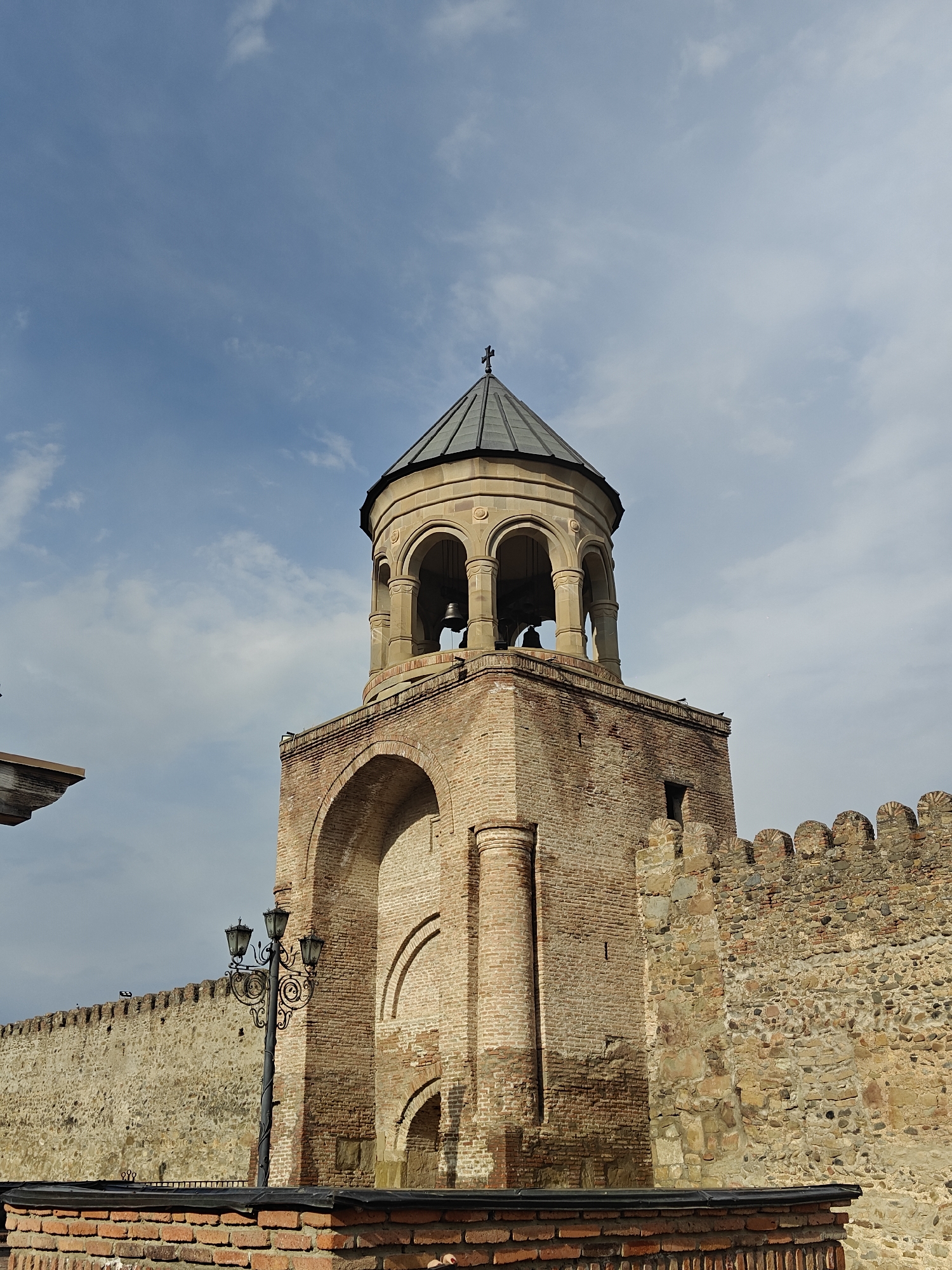 Historic bell tower and fortified wall documented under cloudy skies